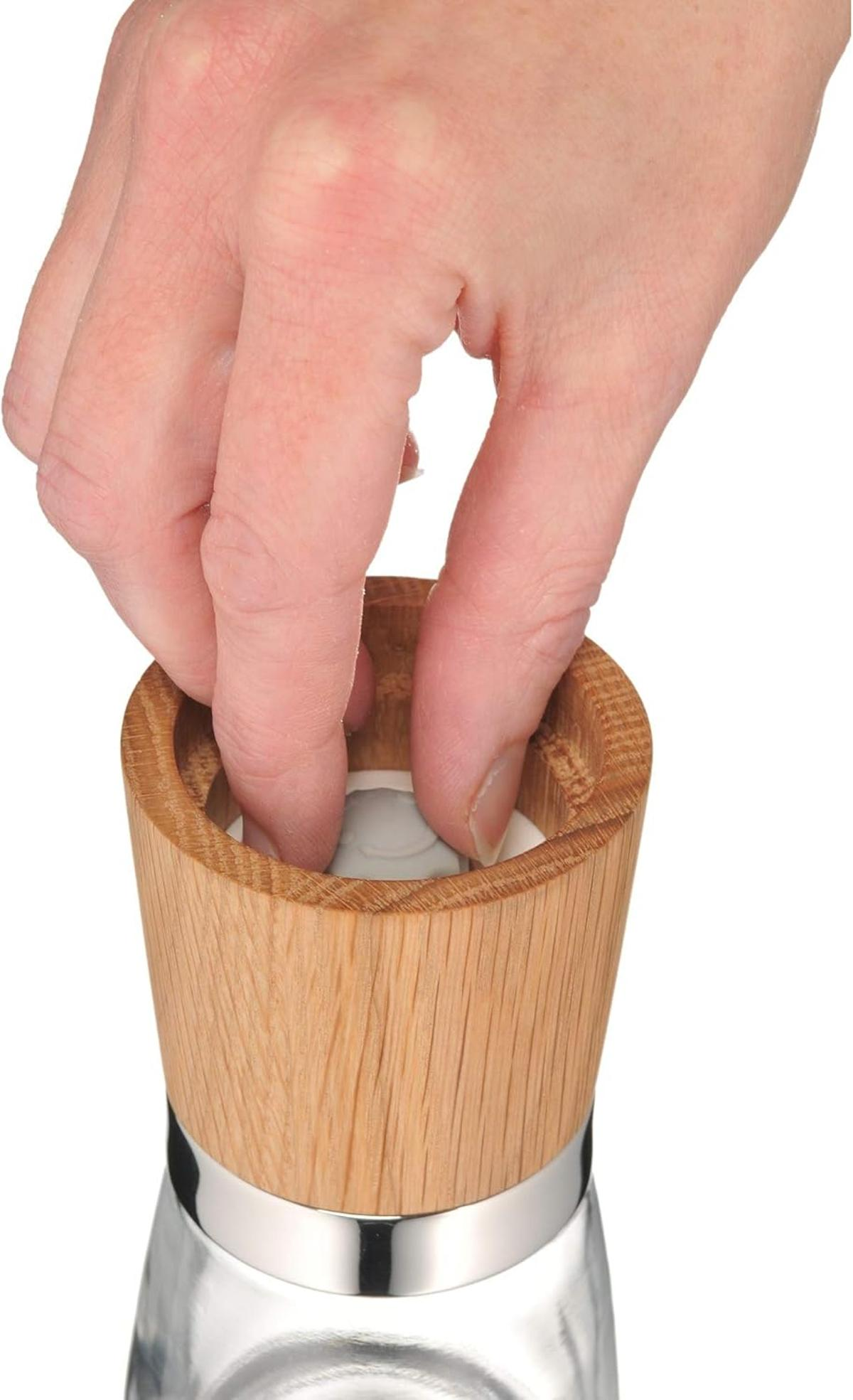 Eine Hand steckt Finger in einen zylindrischen Gegenstand aus Holz. Der Gegenstand hat einen Glassockel und einen Silberring.