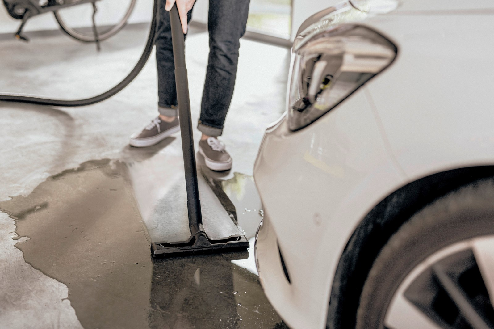 Persona che aspira un pavimento bagnato del garage accanto a un'auto bianca. Una bicicletta è sullo sfondo.