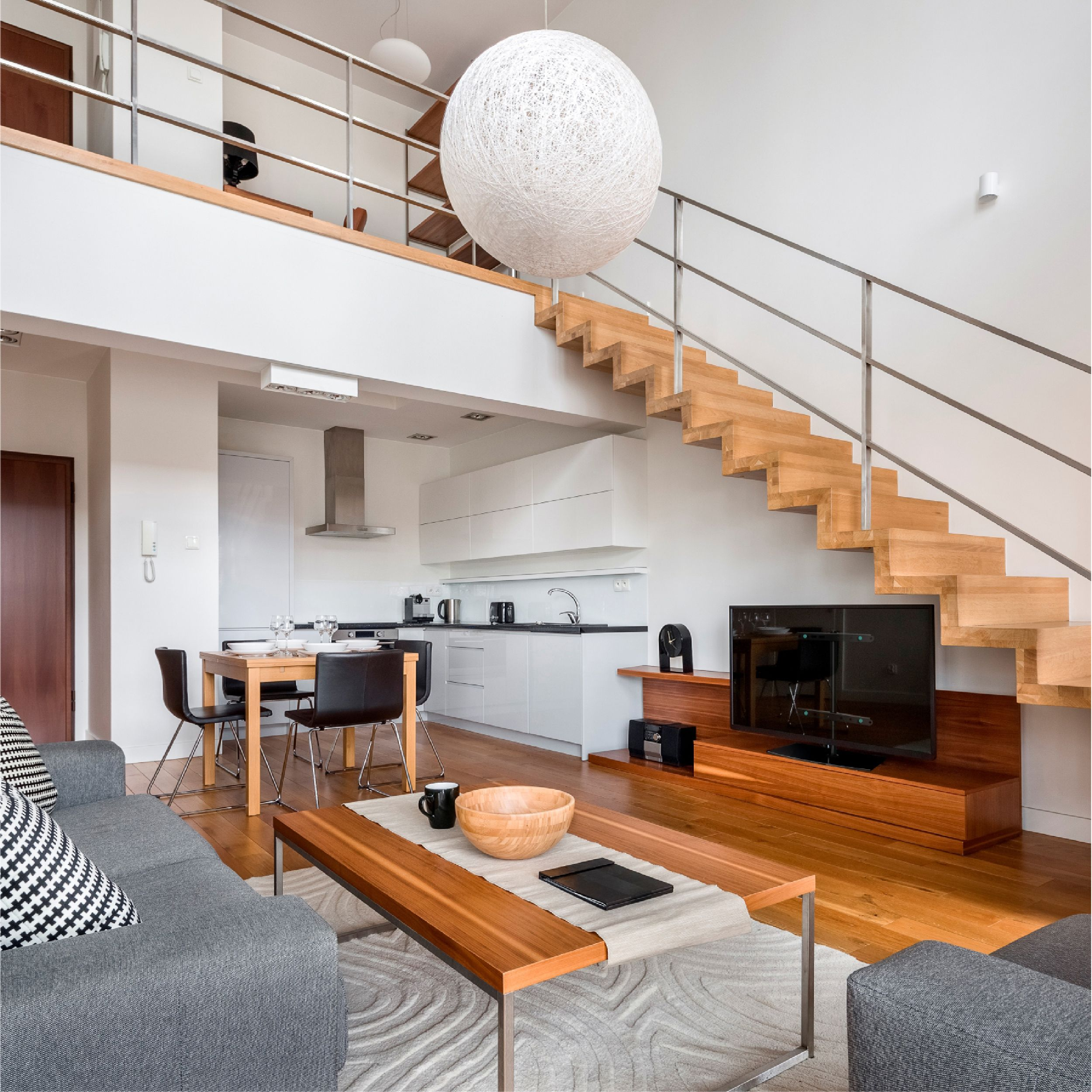 Interni moderni con scala in legno, TV, divano e cucina. Un grande lampadario bianco è appeso sopra il soggiorno.