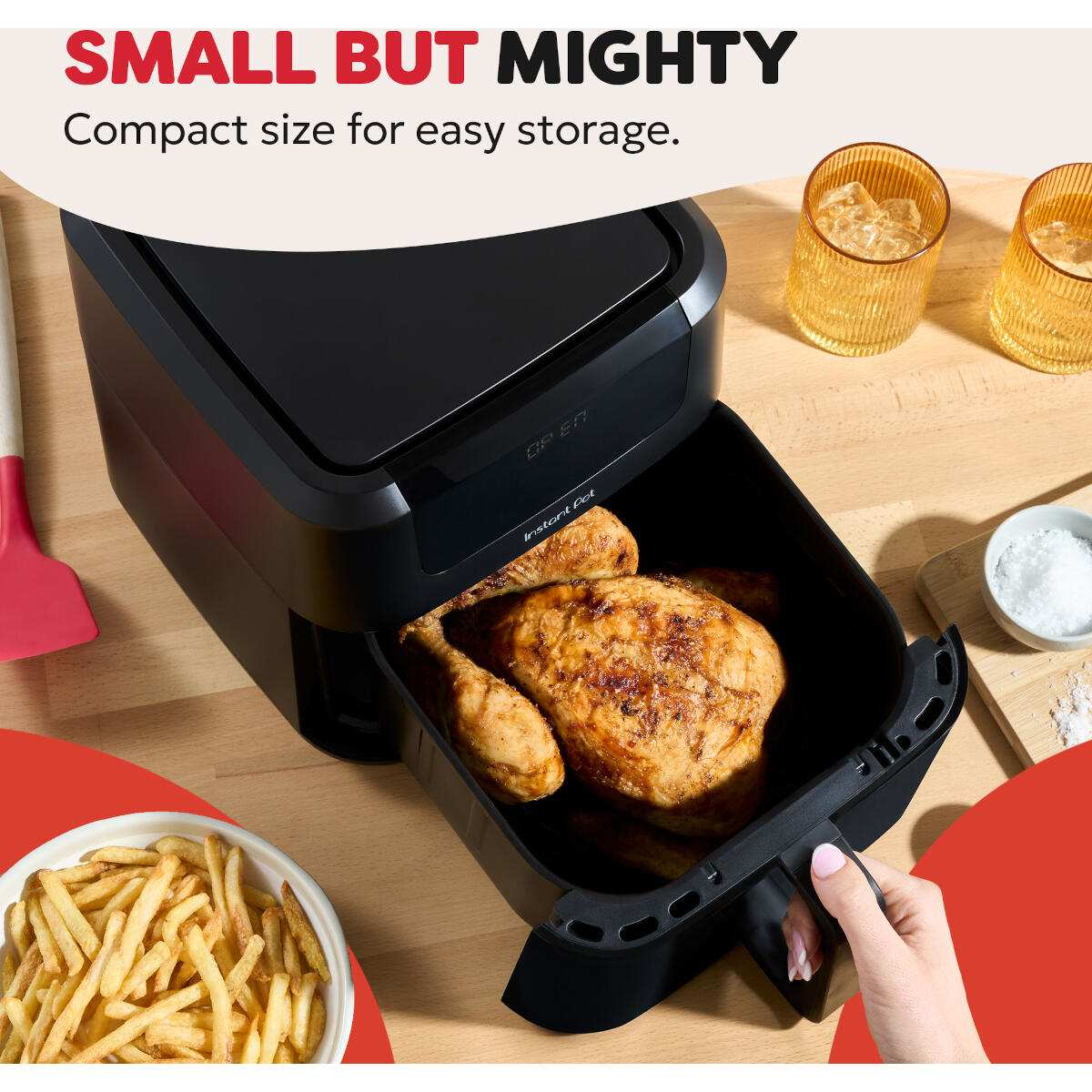 Een airfryer met een gebraden kip erin, friet en een hand die de lade eruit trekt. Twee glazen met ijsblokjes.