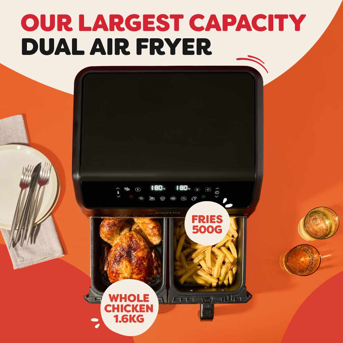Zwarte dubbele airfryer met hele kip en friet. Twee glazen drank rechts en bord met vork en messen links.