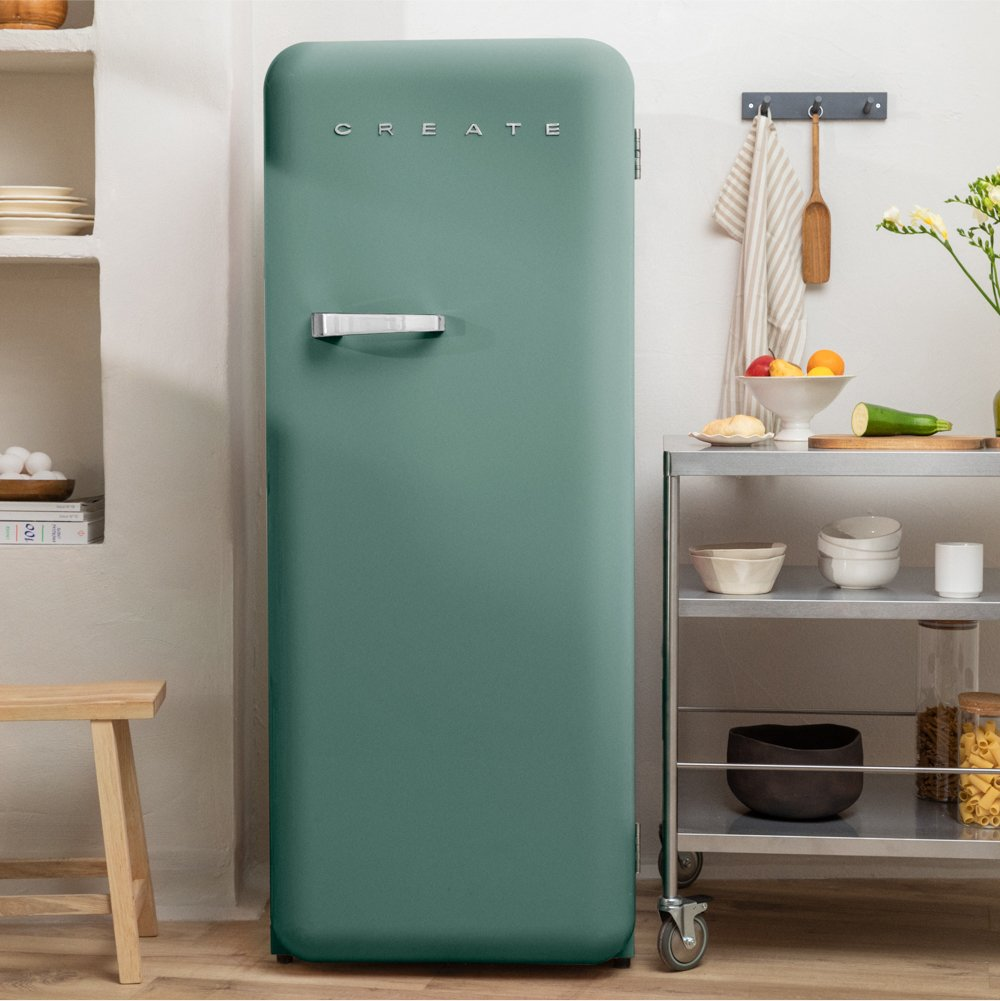 Un refrigerador verde azulado en una cocina. Un estante de metal con cuencos, fruta y calabacín. Un taburete de madera y estantes a la izquierda.