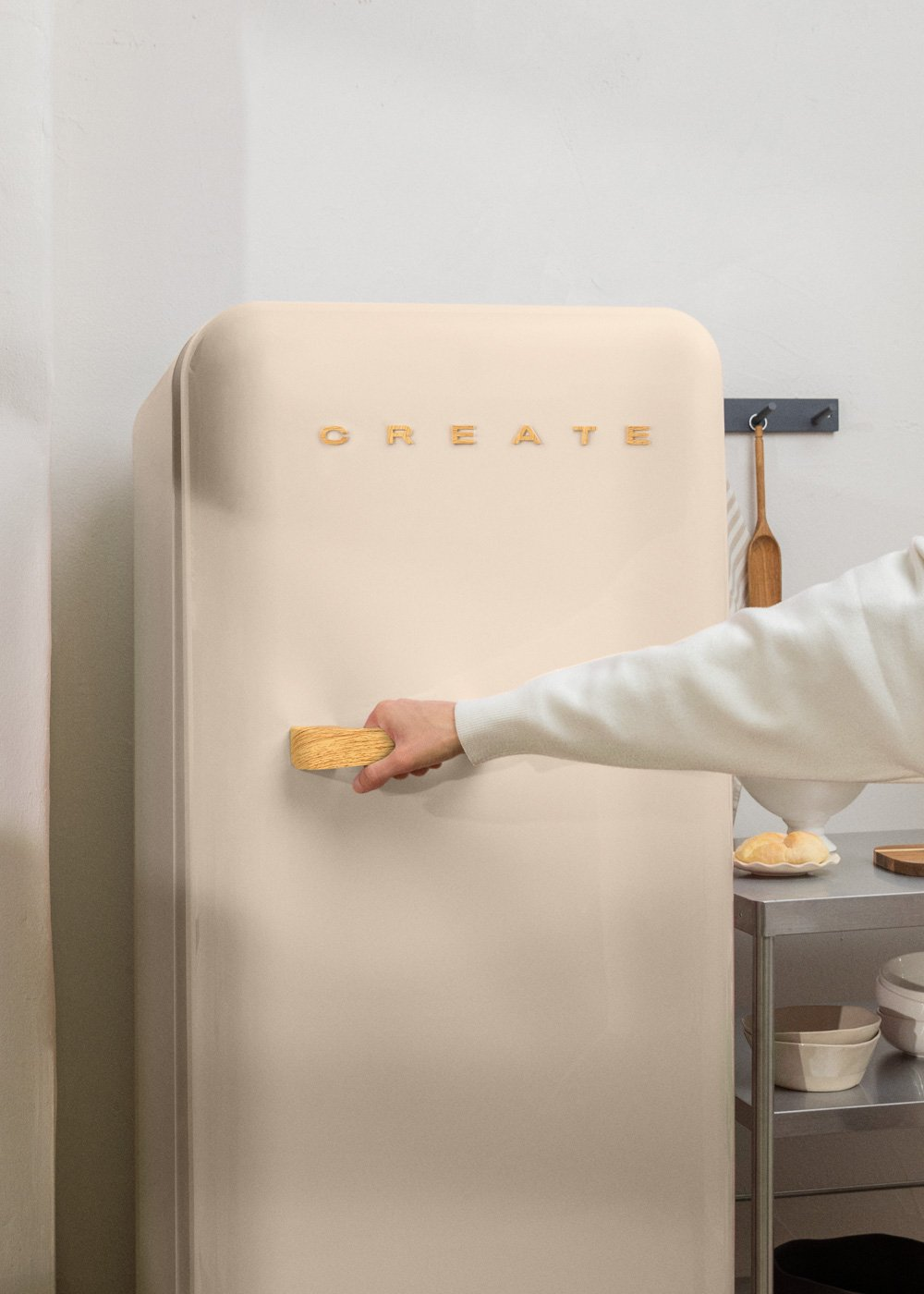 Una persona abre un refrigerador beige. La palabra 'CREATE' está en la puerta. Hay un mango de madera en la puerta.