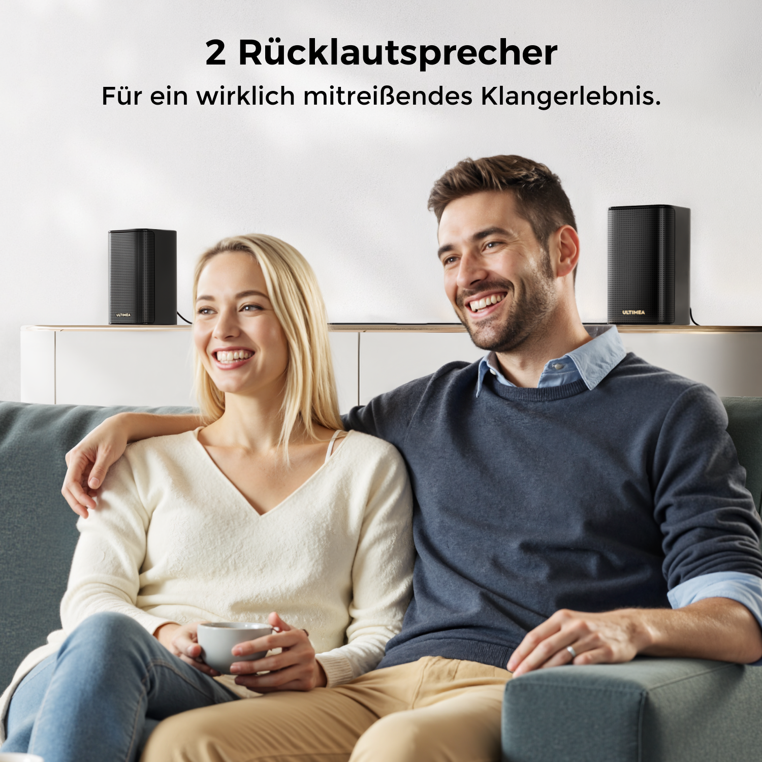 Ein lächelndes Paar auf dem Sofa, zwei schwarze Lautsprecher im Hintergrund. Die Frau hält eine Tasse. Text: '2 Rücklautsprecher'.