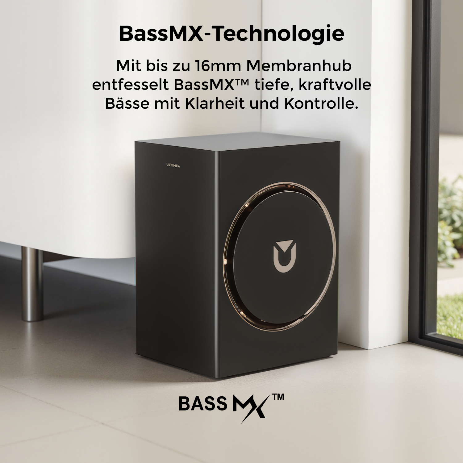 Ein schwarzer Subwoofer mit goldenem Ring und Logo steht neben einer weißen Wand und einem Fenster. Text: BassMX Technologie, BassMX.