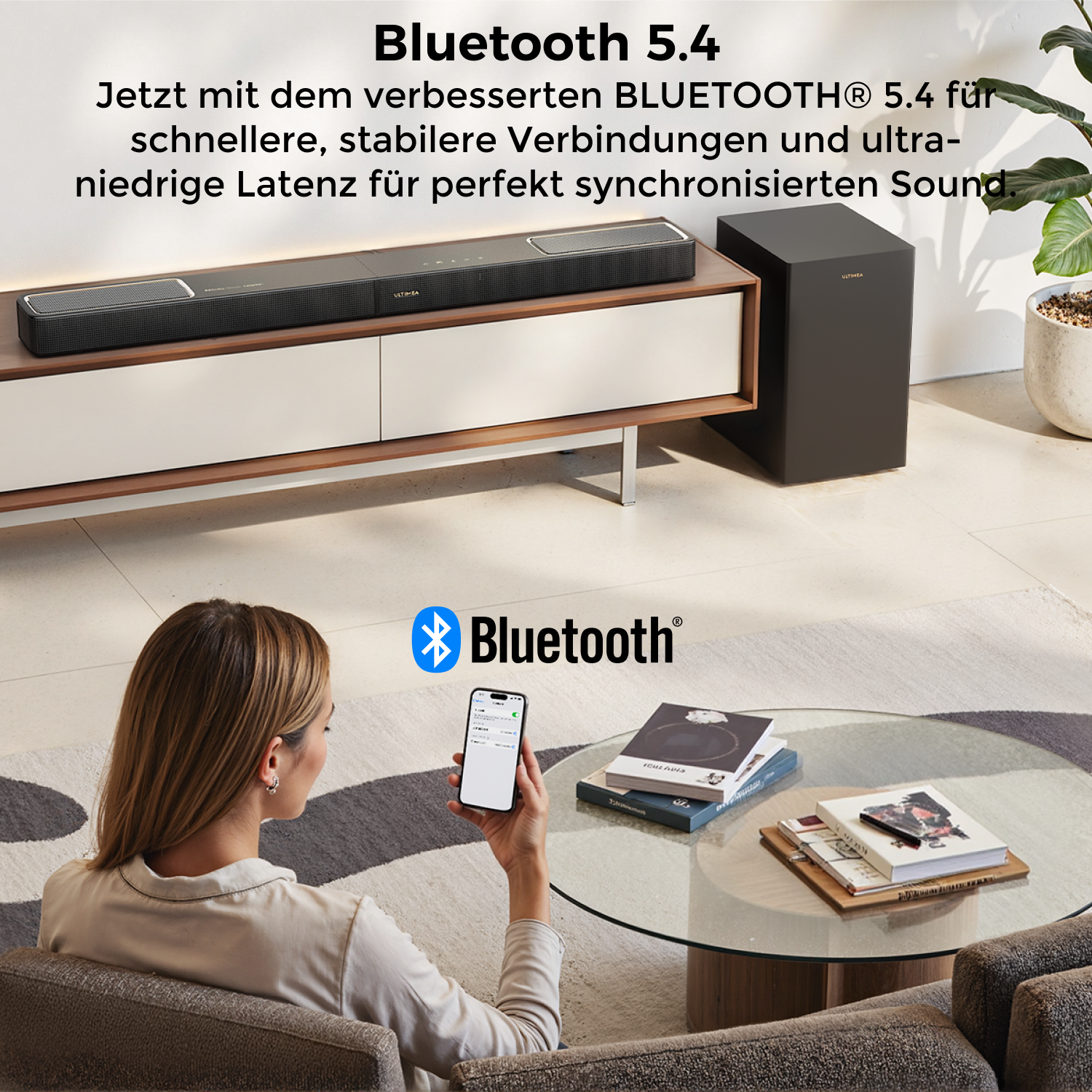 Eine Frau hält ein Telefon in der Nähe eines Tisches mit Büchern. Eine Soundbar und ein Subwoofer stehen auf einem Schrank. Bluetooth-Logo sichtbar.