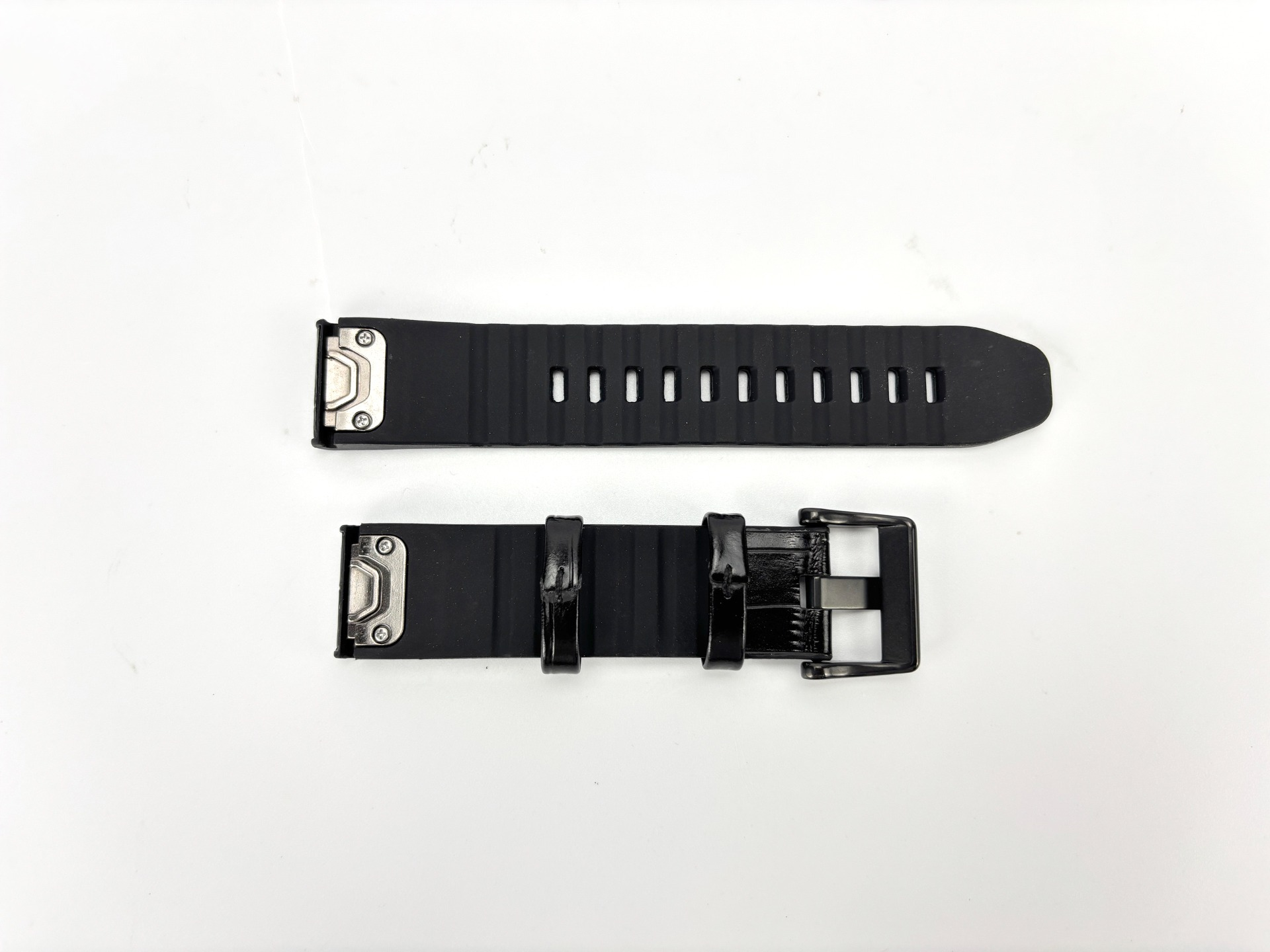 Zwei schwarze Uhrenarmbänder auf weißem Untergrund. Eines ist ein Einzelstück mit Löchern, das andere hat eine Schnalle und zwei Schlaufen.
