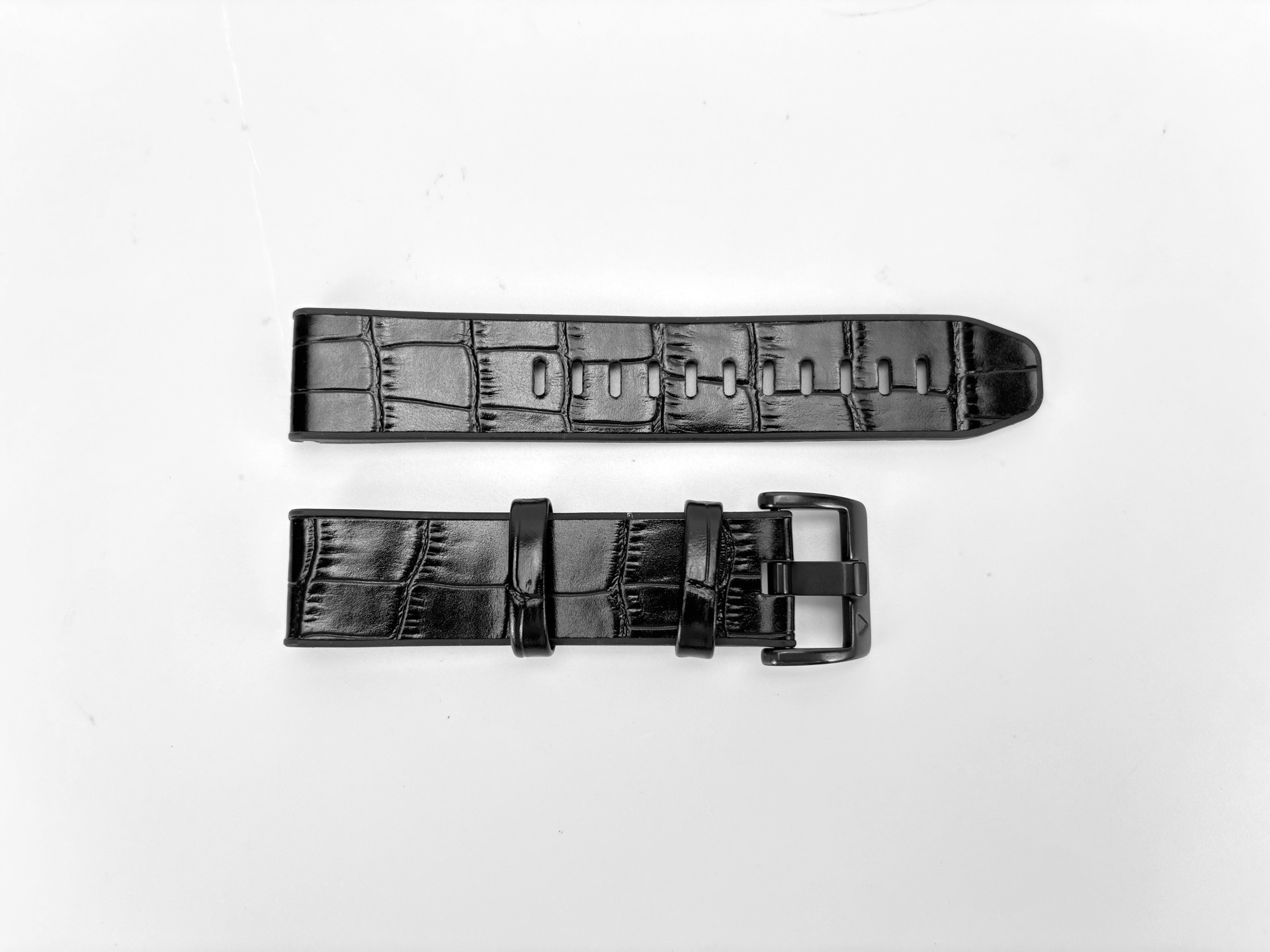 Zwei schwarze Leder-Armbänder auf weißem Untergrund. Ein Band hat Löcher, das andere eine Schnalle.