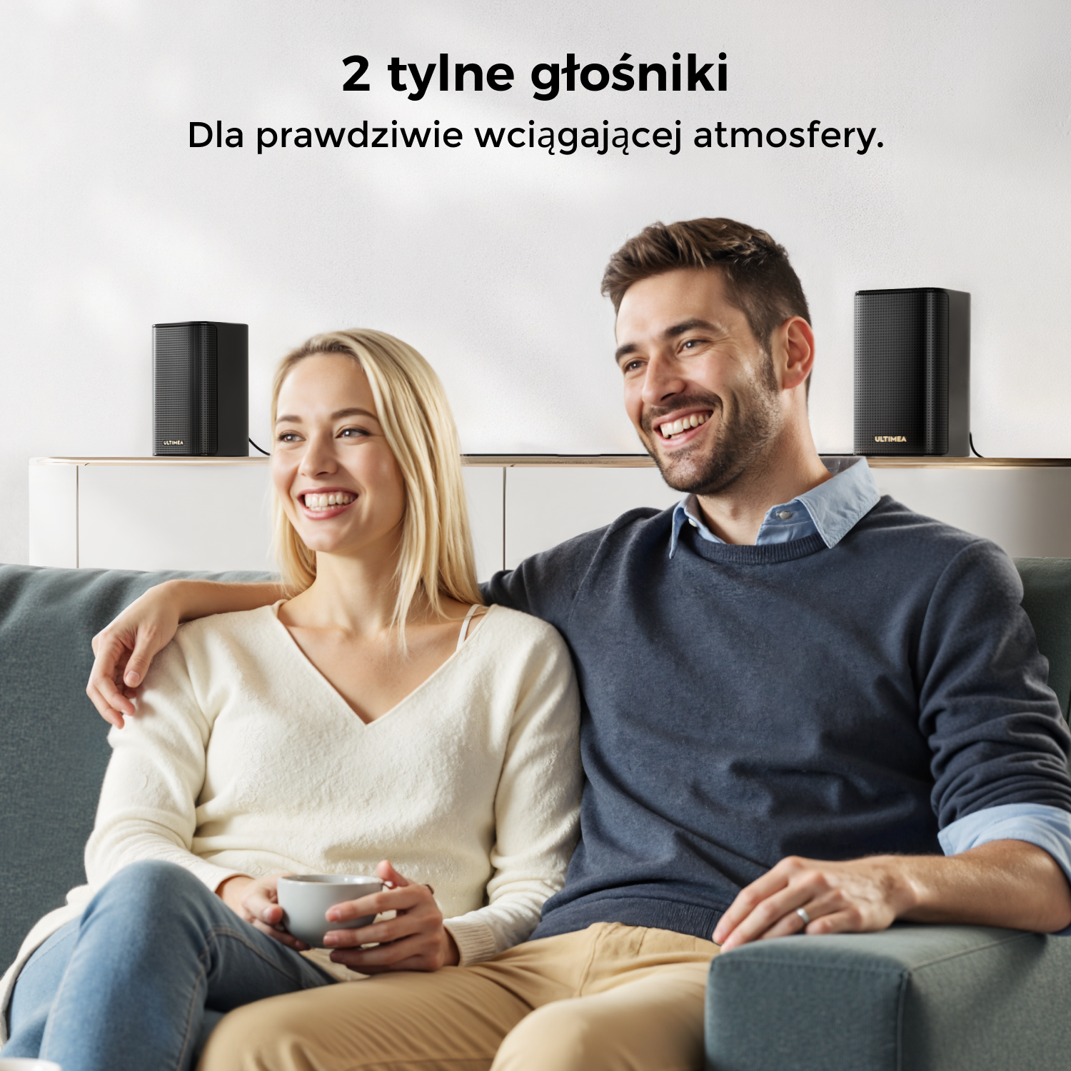 Para uśmiecha się na kanapie z dwoma czarnymi głośnikami. Tekst: 2 tylne głośniki dla wciągającej atmosfery.