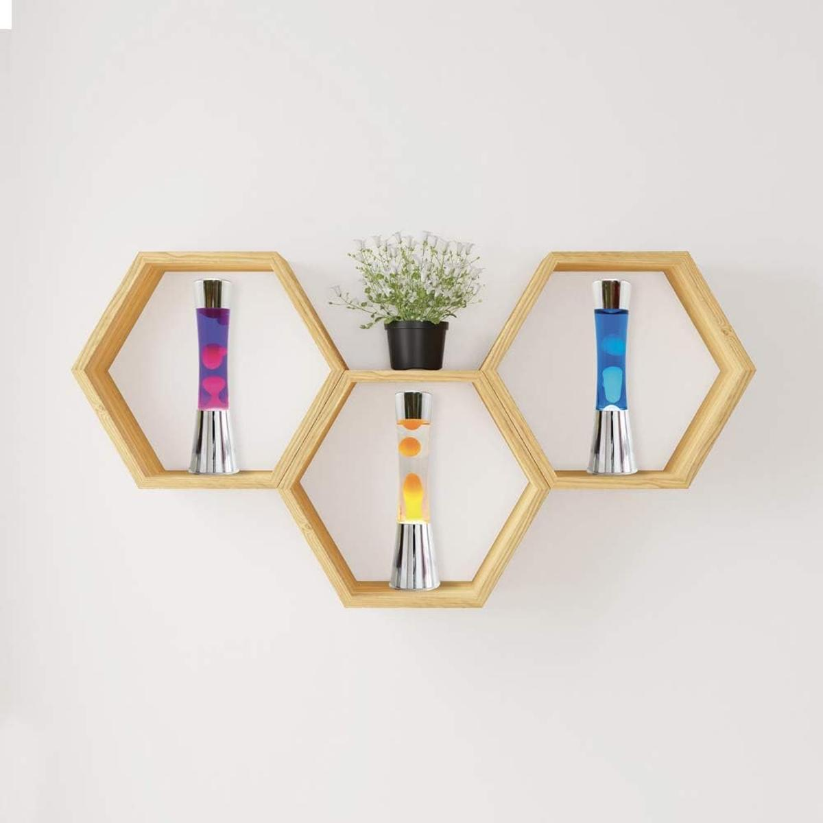 Sechseckige Holzregale mit Lavalampe in Pink, Orange und Blau und einer Topfpflanze vor einer weißen Wand.