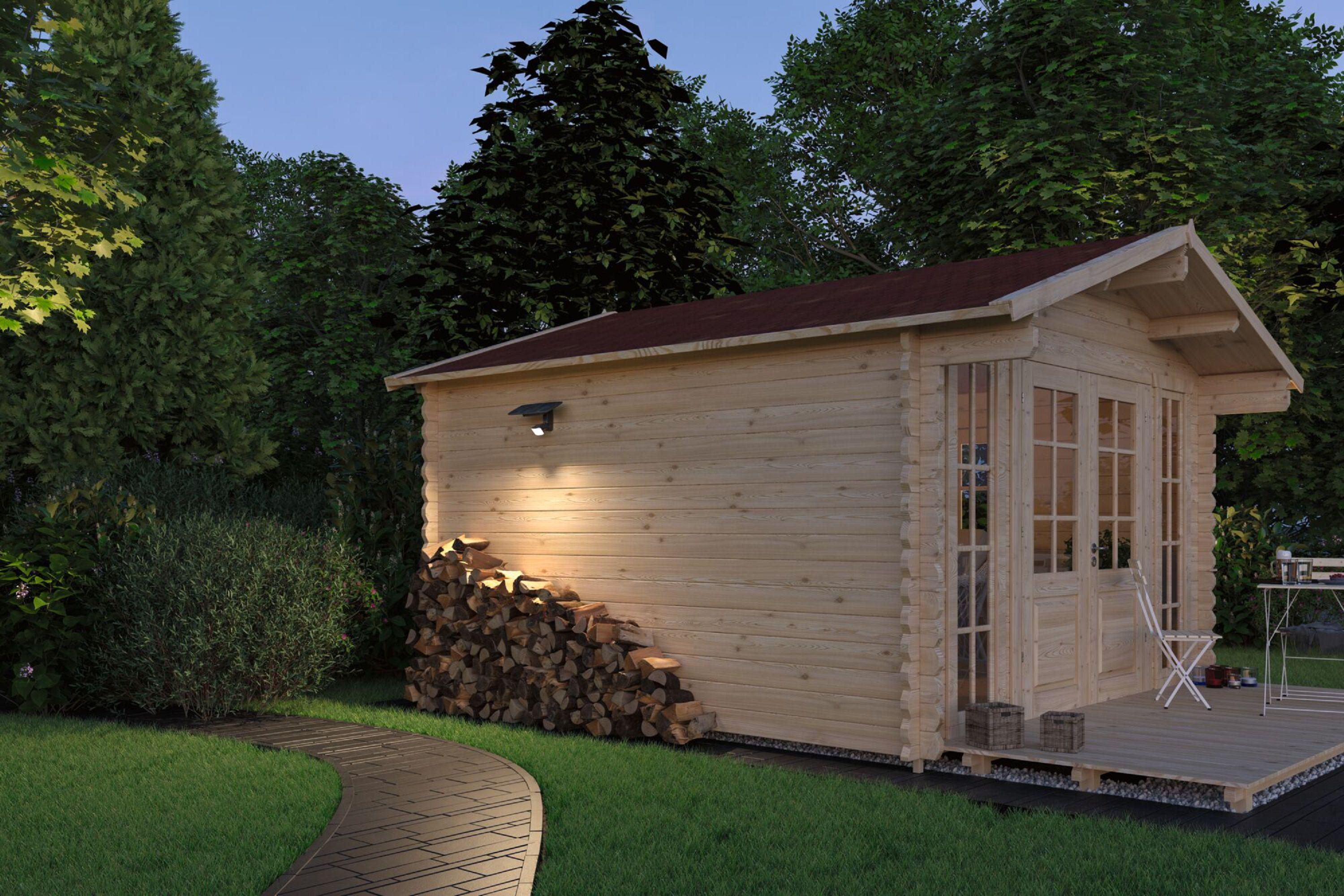 Drewniana kabina ze stosami drewna opałowego, oświetlona światłem słonecznym. Zielone drzewa otaczają kabinę, ścieżka na pierwszym planie.