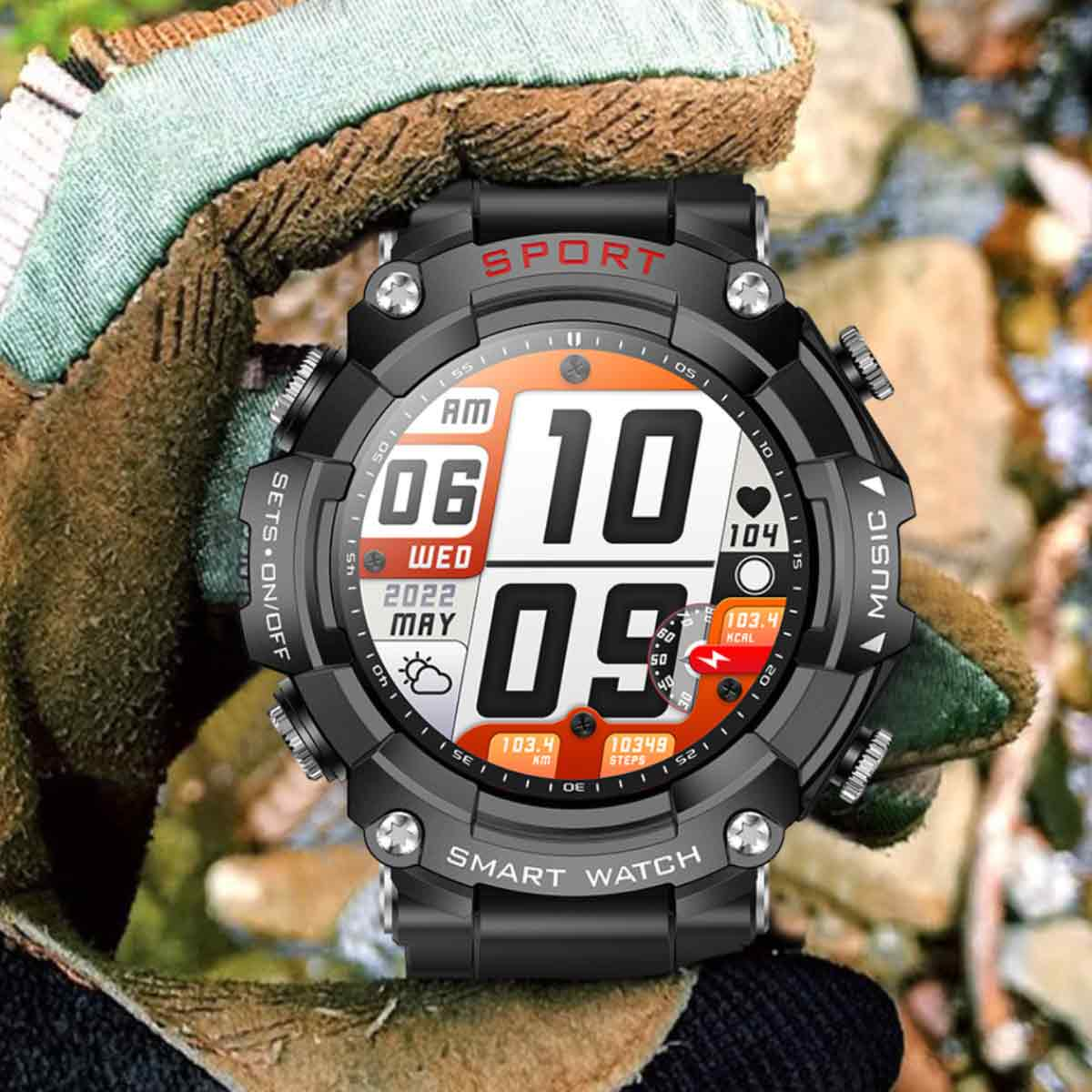Eine schwarze Smartwatch zeigt Uhrzeit, Datum und Fitness-Metriken an. Sie wird von einer behandschuhten Hand vor einem verschwommenen, felsigen Hintergrund gehalten.