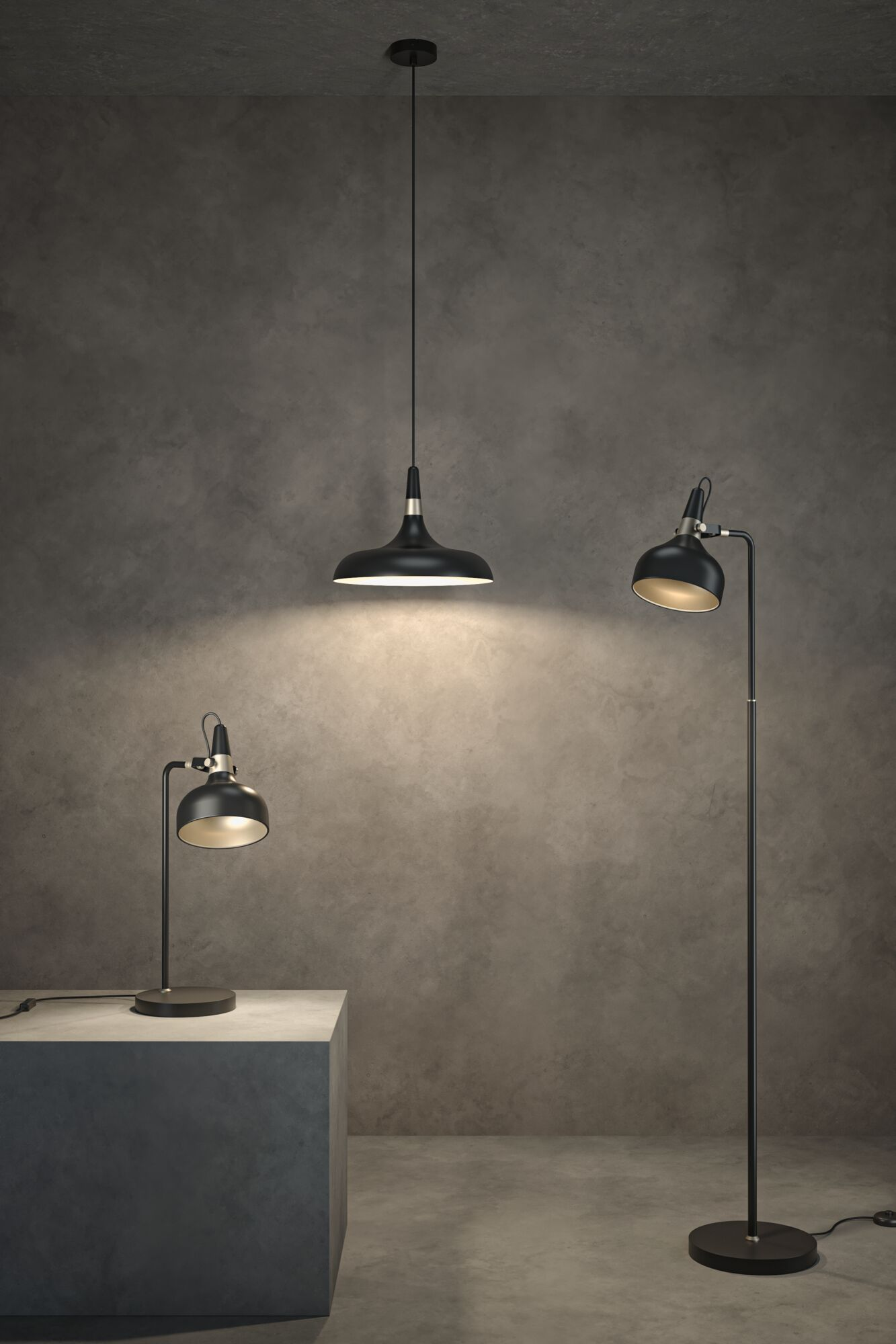 Drei schwarze Lampen: eine Pendelleuchte, eine Tischlampe und eine Stehlampe. Sie stehen vor einer grauen Wand. Das Licht ist in allen an.