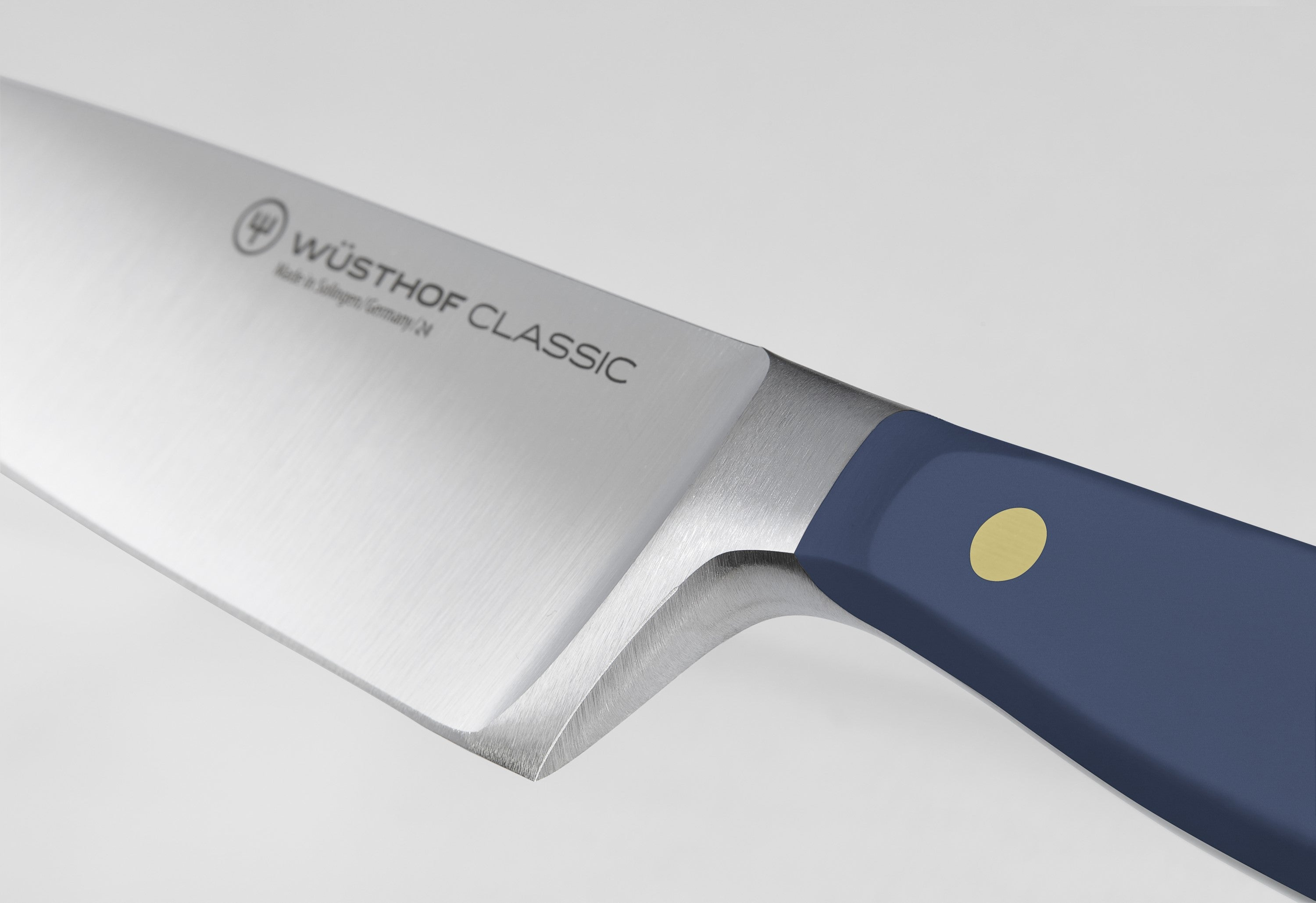 Primer plano de un cuchillo Wüsthof Classic. La hoja es plateada, el mango azul, con un punto dorado. El fondo es blanco.
