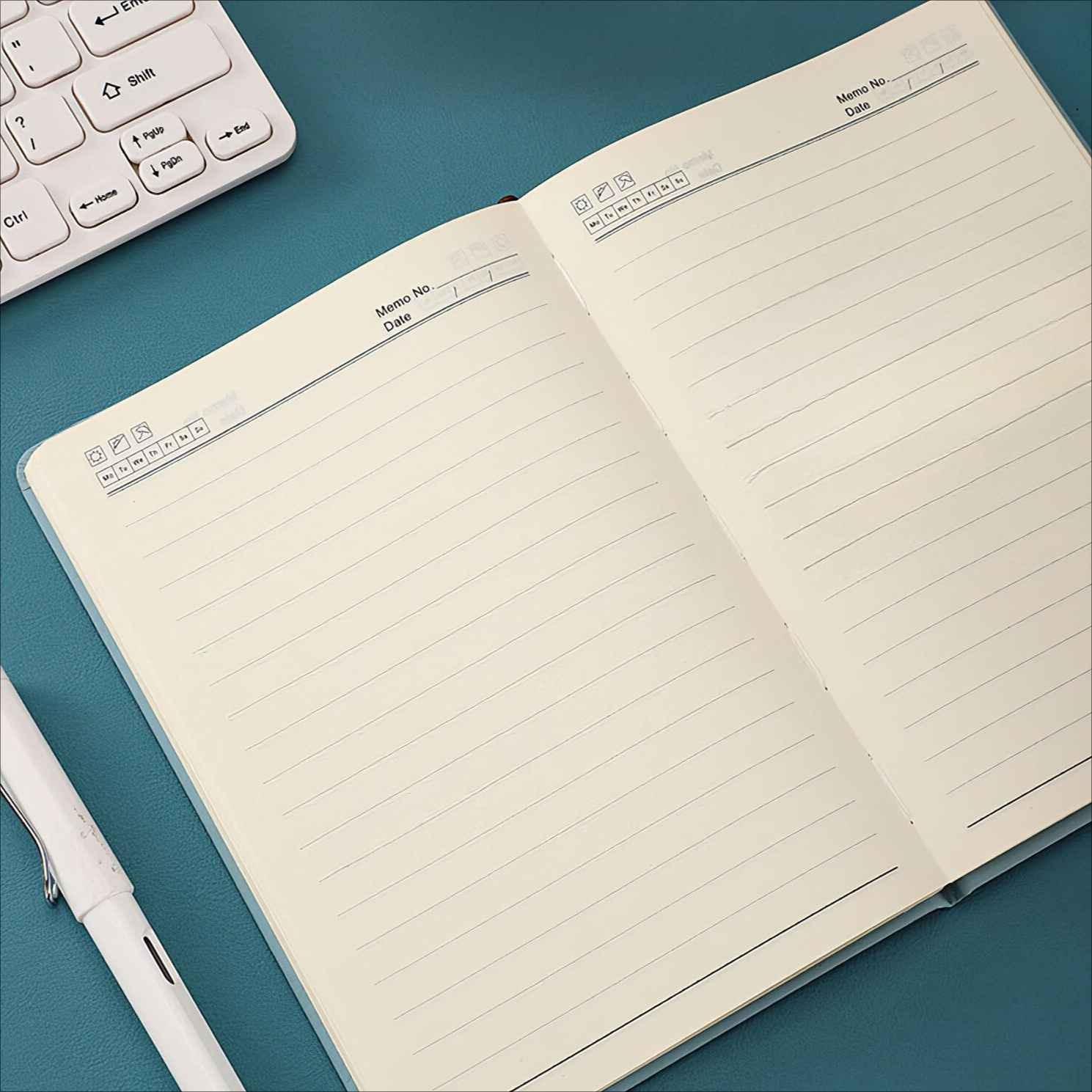 Ein offenes Notizbuch mit linierten Seiten liegt auf einer blauen Oberfläche. Ein weißer Stift und eine Tastatur sind ebenfalls zu sehen.