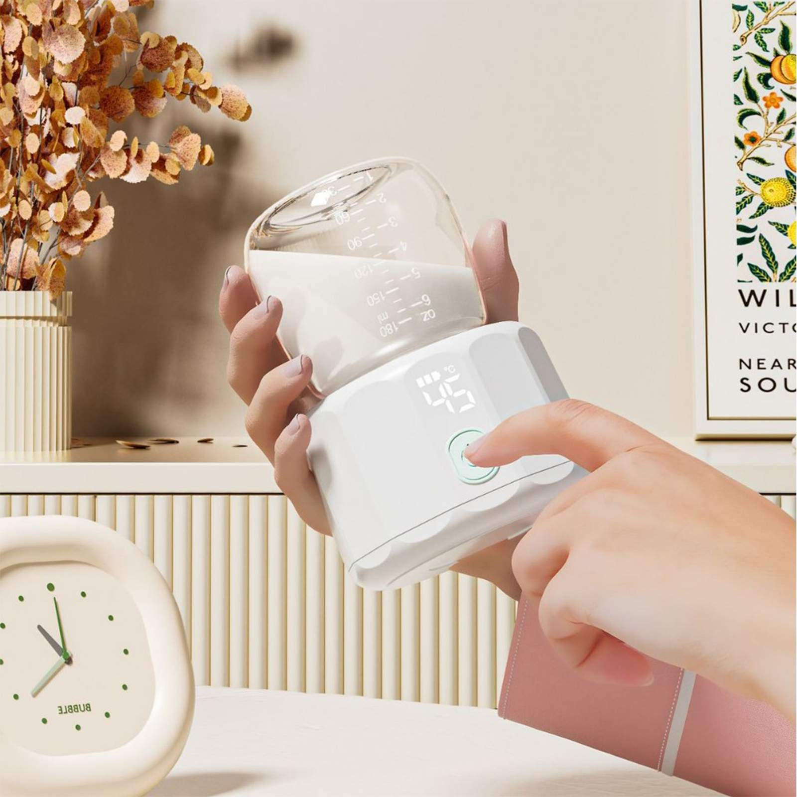 Hände halten eine Babyflasche mit Milch. Ein Finger drückt einen Knopf an einem weißen Gerät, Hintergrund mit Blumen und Uhr.