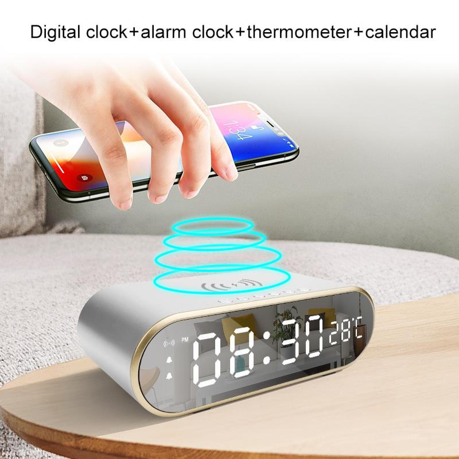 Eine Hand hält ein Telefon über einer Digitaluhr. Die Uhr zeigt Zeit und Temperatur auf einem Tisch an.