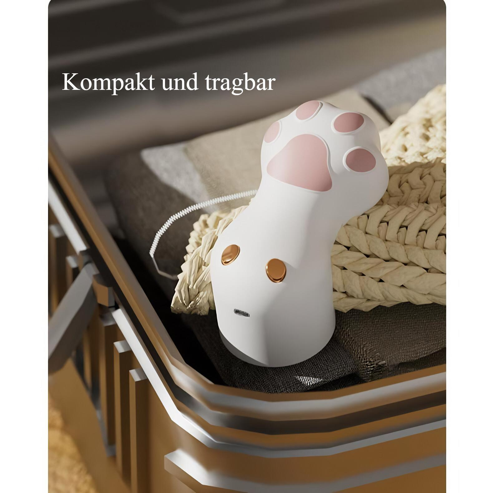Ein weißes, pfotenförmiges Gerät mit rosa Pads und goldenen Knöpfen liegt in einer Schublade auf strukturiertem Stoff.