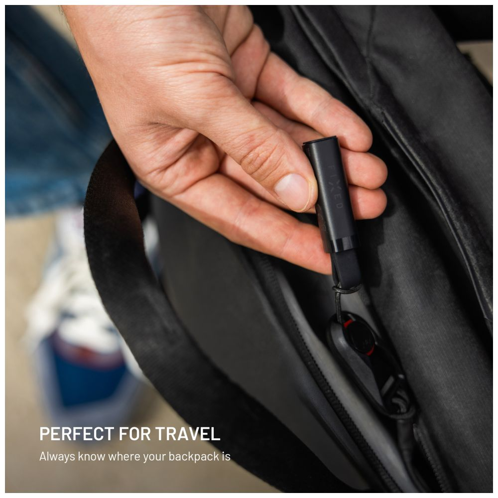 Eine Hand steckt einen schwarzen Tracker in eine Rucksacktasche. Der Tracker ist mit FIXED beschriftet. Der Text lautet: 'PERFEKT FÜR REISEN'.