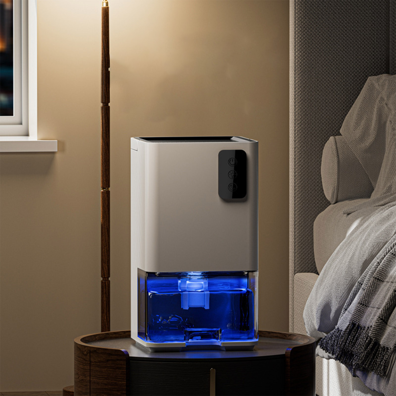 Ein weißer Luftentfeuchter mit blau leuchtendem Wassertank steht auf einem Nachttisch. Im Hintergrund befindet sich ein Bett mit einer Decke.