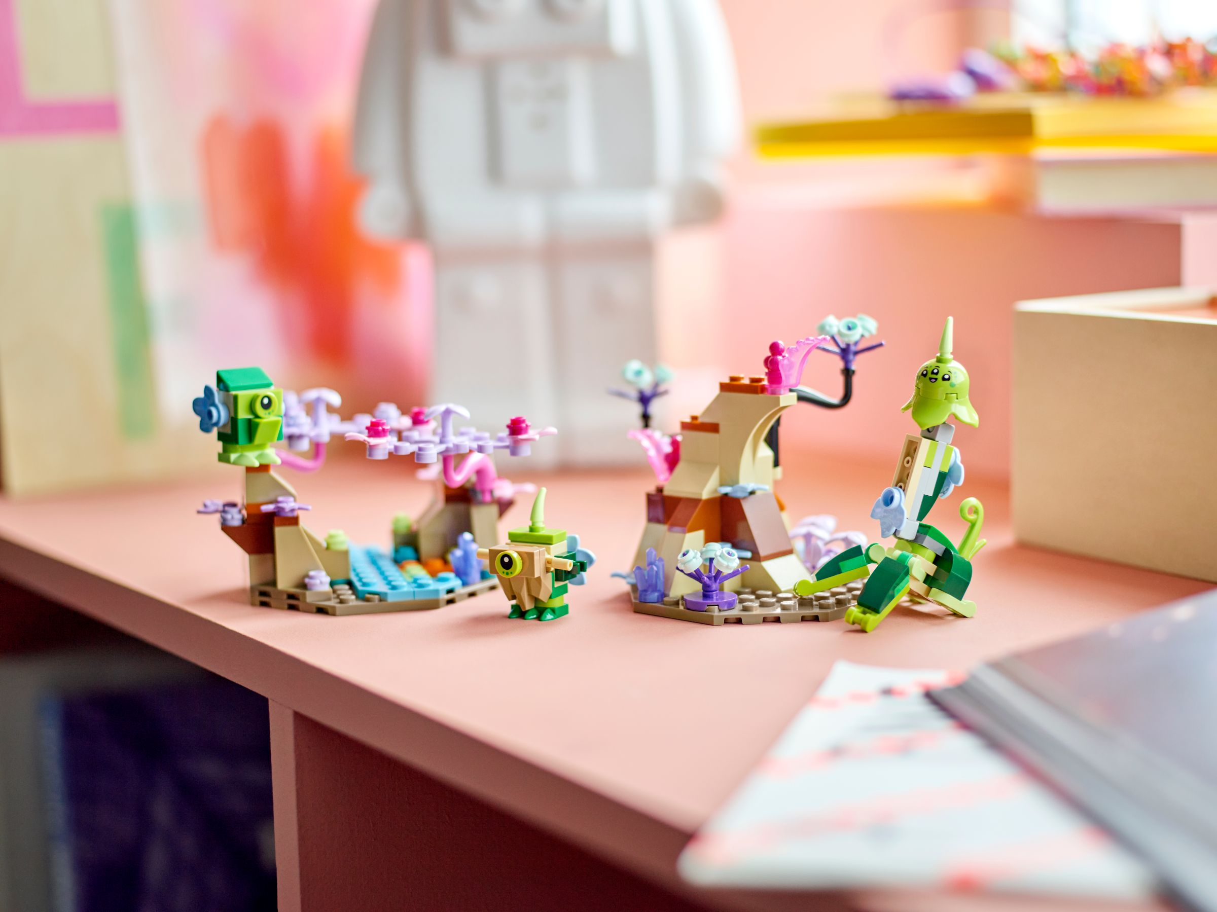 Eine rosa Oberfläche mit Lego-Figuren. Die Figuren sind grün und braun. Der Hintergrund ist verschwommen mit Weiß und Rosa.