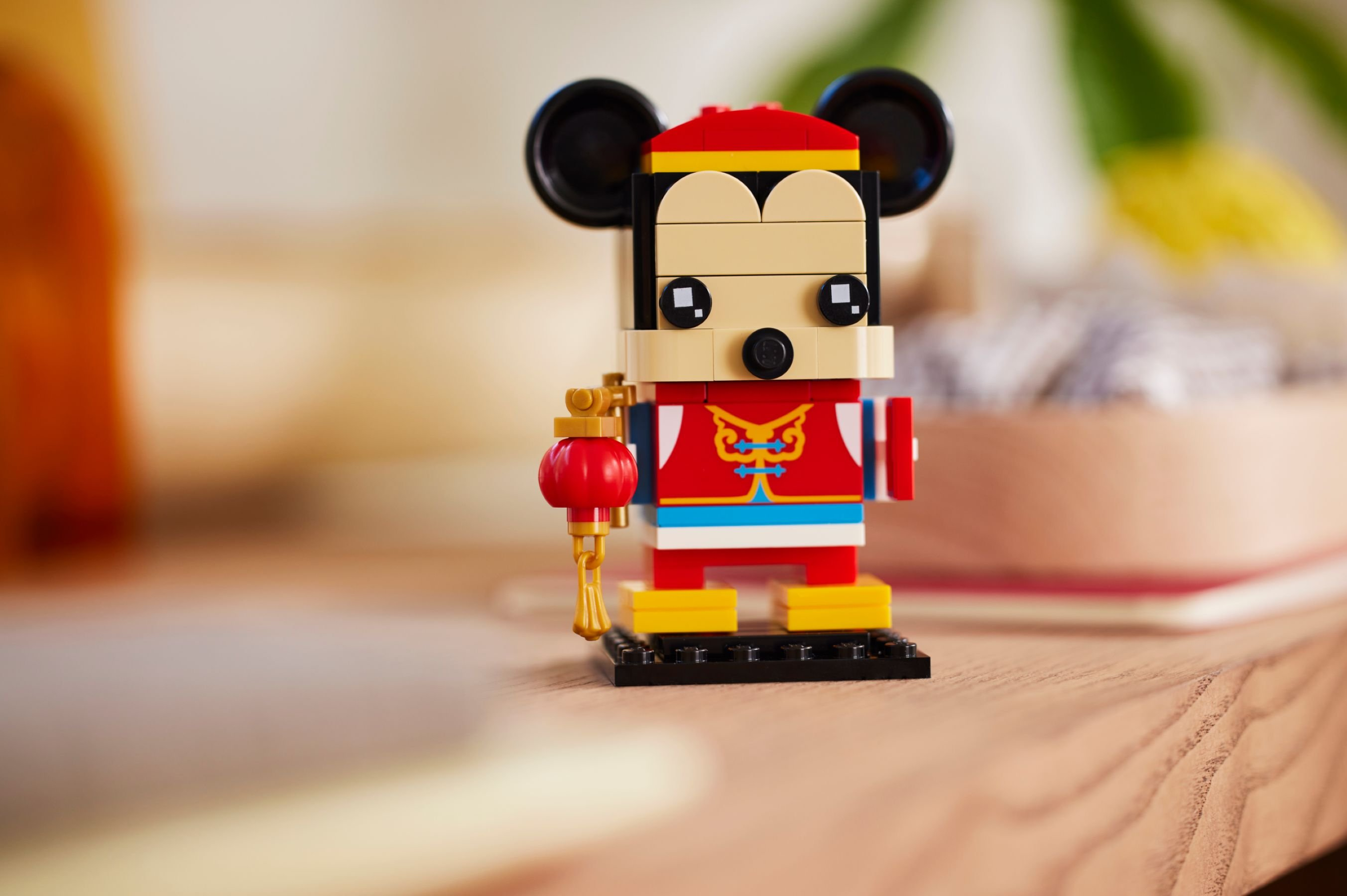 Eine Lego-Mausfigur mit roter, gelber und blauer Kleidung, die eine Laterne hält. Sie steht auf einer schwarzen Basis.