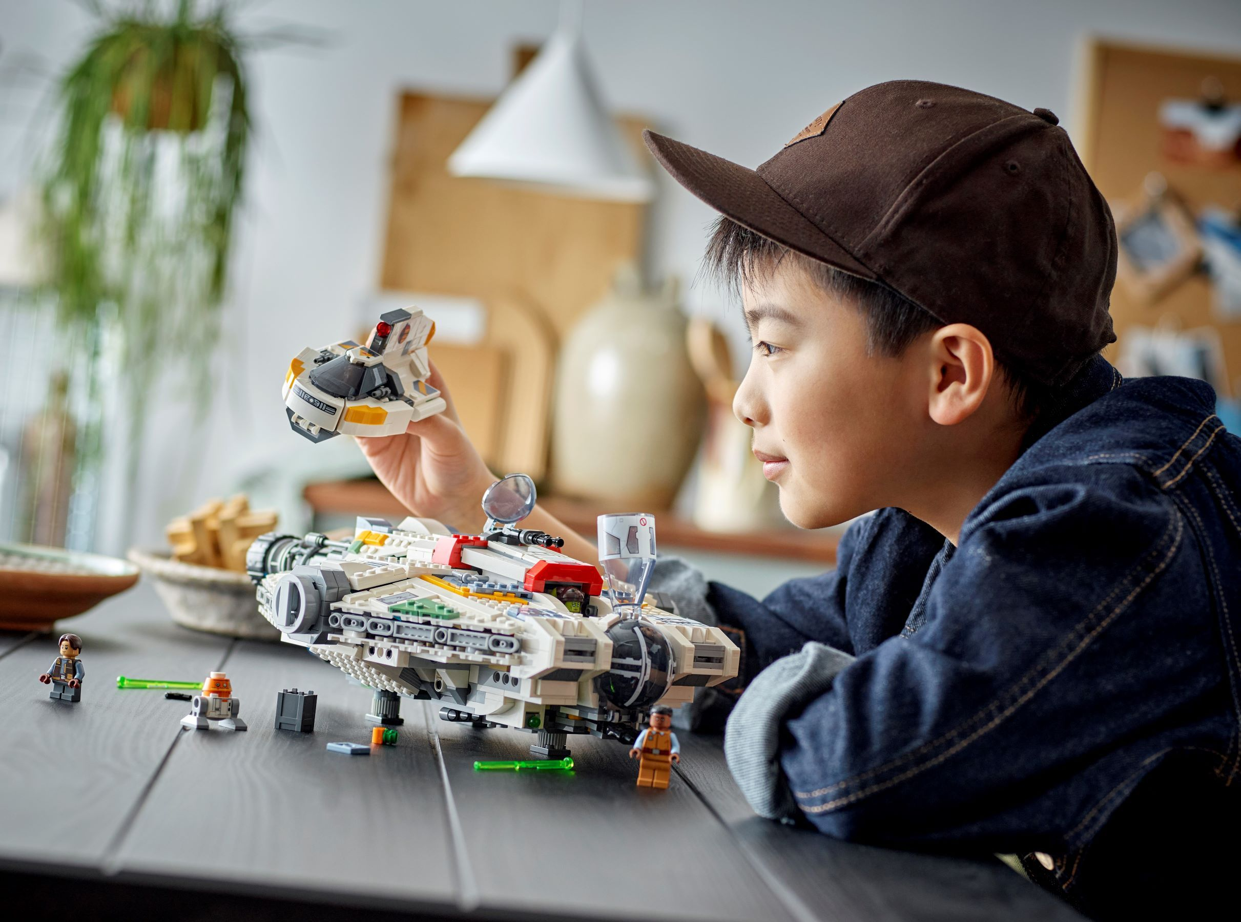 Chłopiec w czapce bawi się zestawem Lego Star Wars. Lego Sokół Millennium i inne figurki Lego.