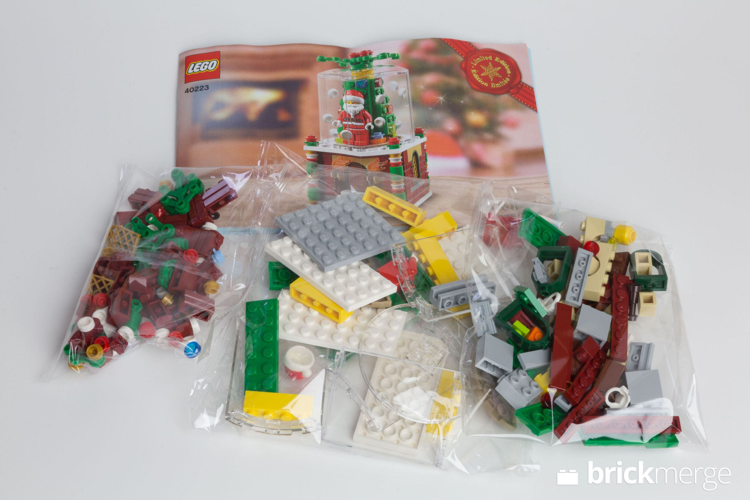 Lego-Set mit Anleitung und Weihnachtsmannfigur in einer Schneekugel. Tüten mit Lego-Steinen liegen vor der Anleitung.