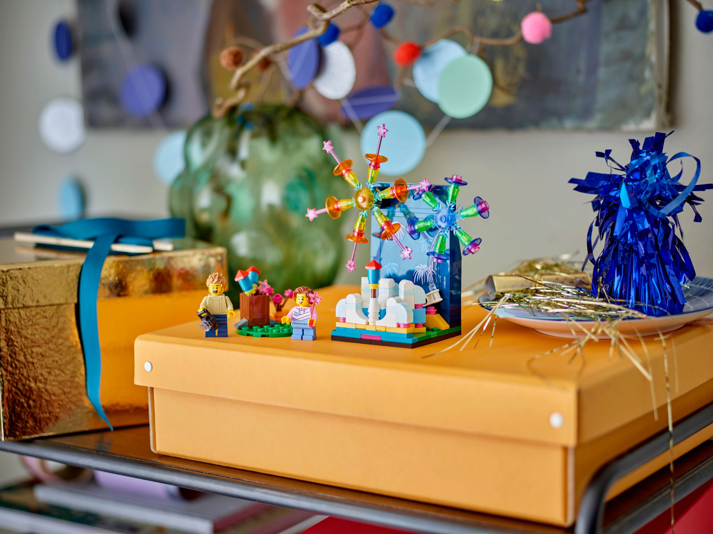 Ein Lego-Riesenrad und Figuren stehen auf einer orangefarbenen Box. Weitere Dekorationen sind ein grüner Kürbis und blaue Folie.