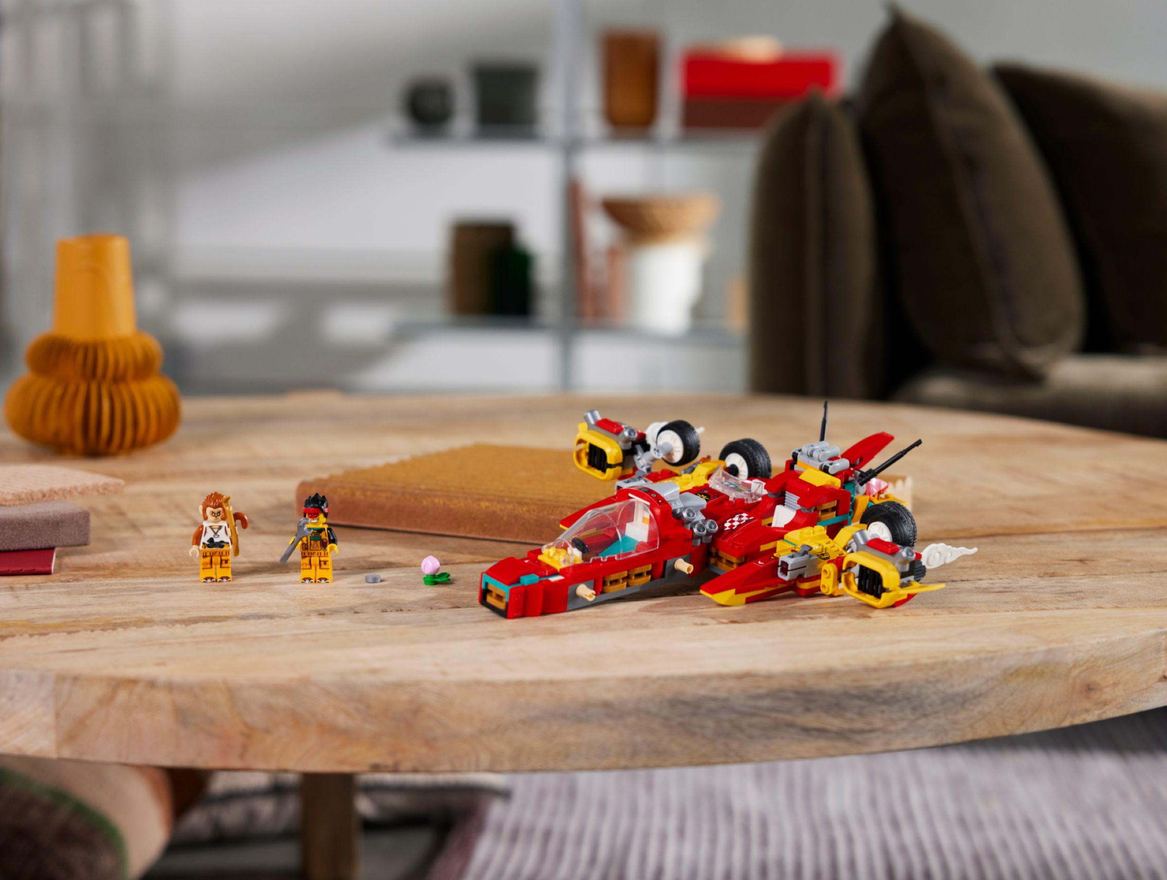 Ein rotes und gelbes Lego-Raumschiff mit zwei Minifiguren auf einem Holztisch, mit verschwommenem Hintergrund.