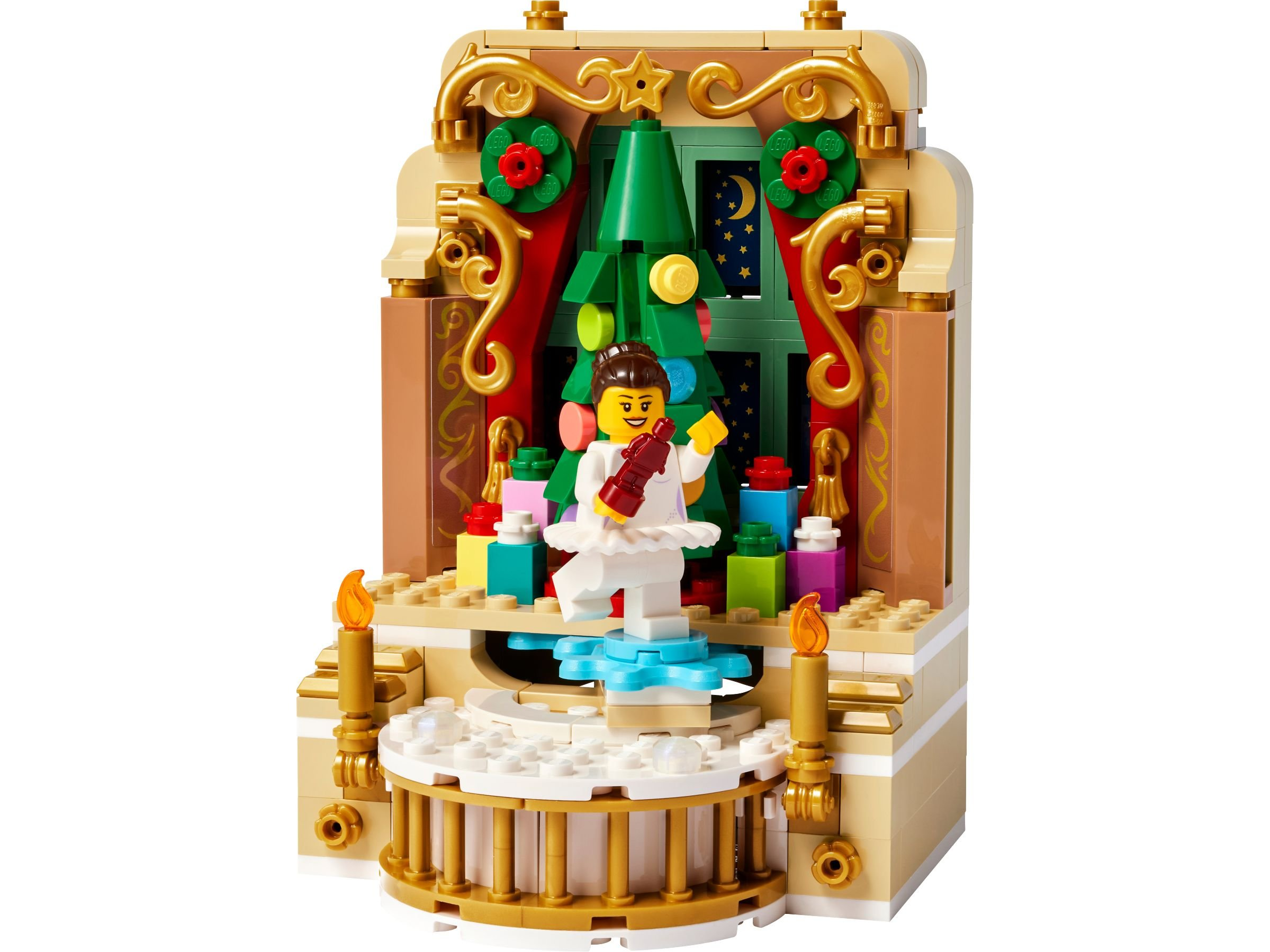 Eine LEGO-Weihnachtsszene mit Ballerina, Weihnachtsbaum, Geschenken und goldenem Rahmen. Zwei Kerzen flankieren die Szene.