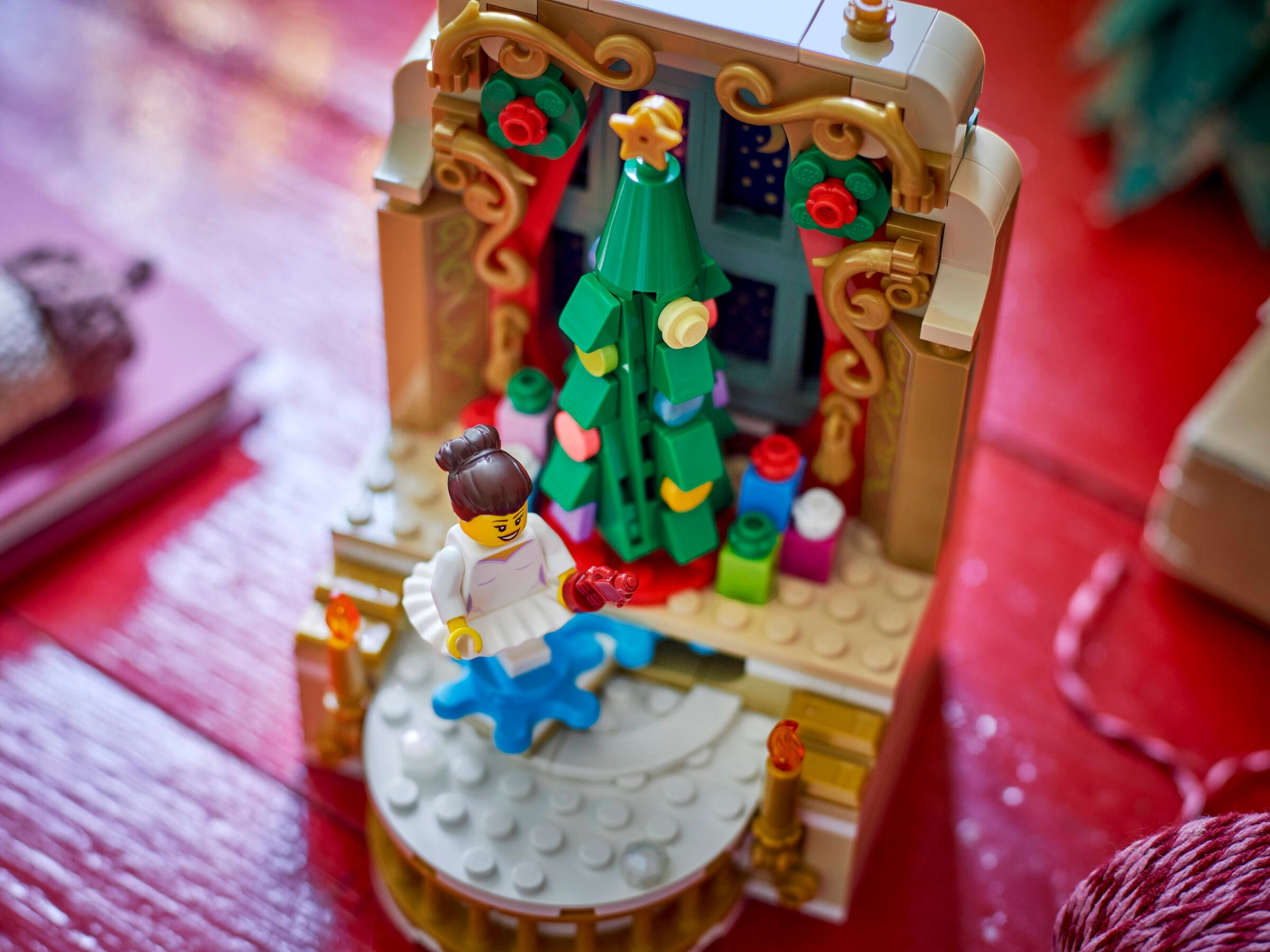 Eine Lego-Weihnachtsszene mit einem geschmückten Baum, einer Lego-Figur und bunten Geschenken auf roter Oberfläche.