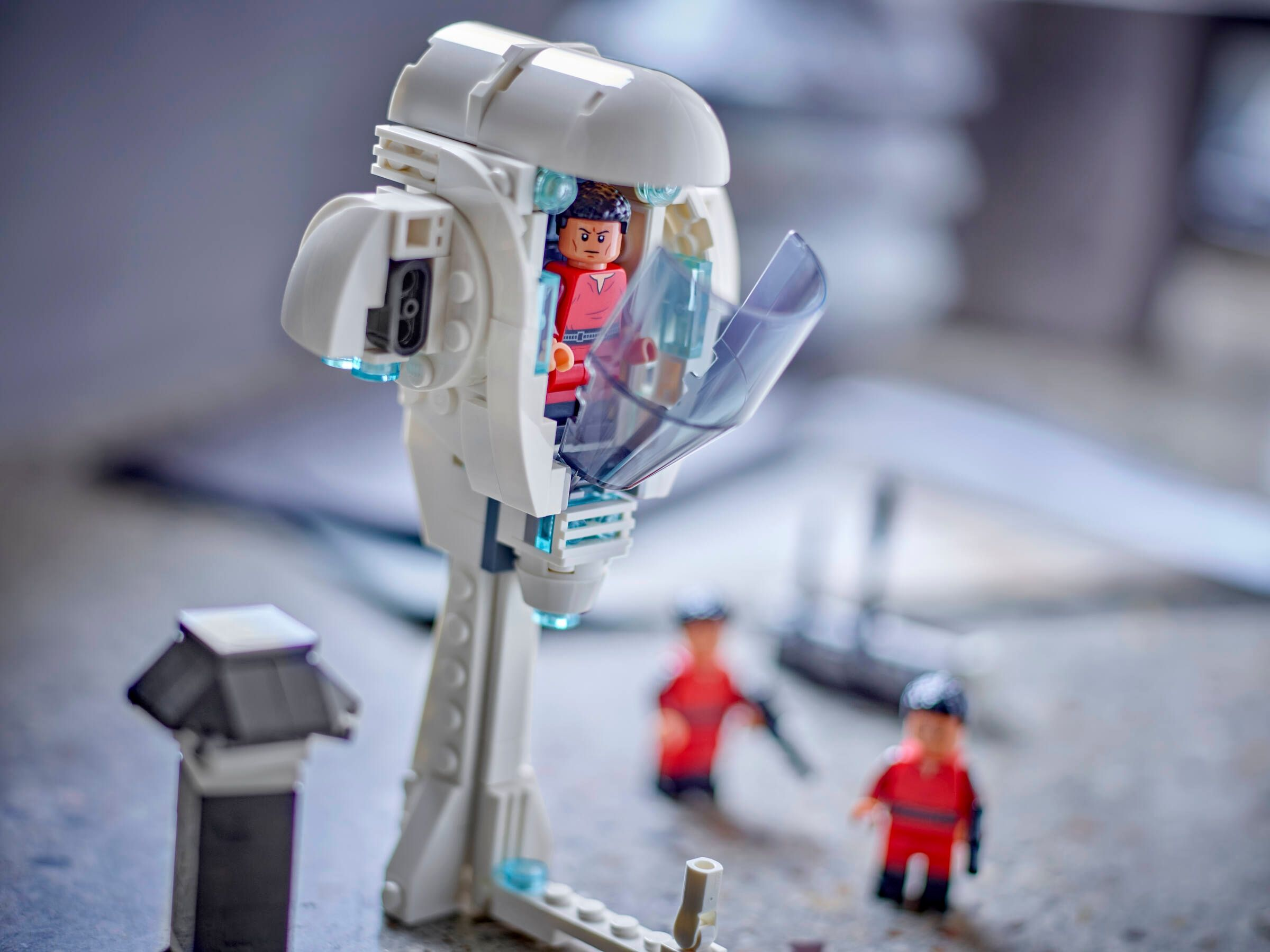 Lego Star Wars Set. Eine weiße Kapsel mit einer Minifigur. Zwei rot gekleidete Figuren stehen im Hintergrund.
