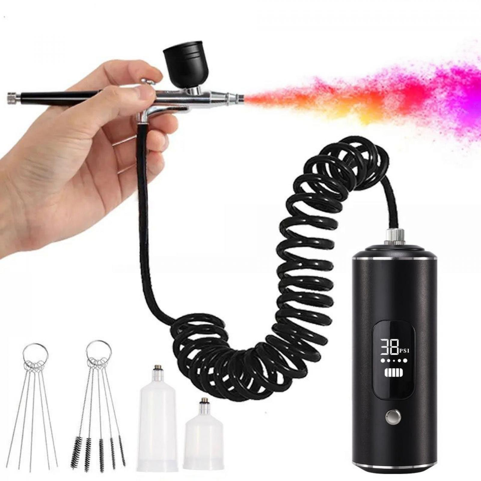 Hand hält Airbrush, die bunten Nebel sprüht. Schwarzer Schlauch und Kompressor, Reinigungswerkzeuge und Flaschen sind ebenfalls im Bild.