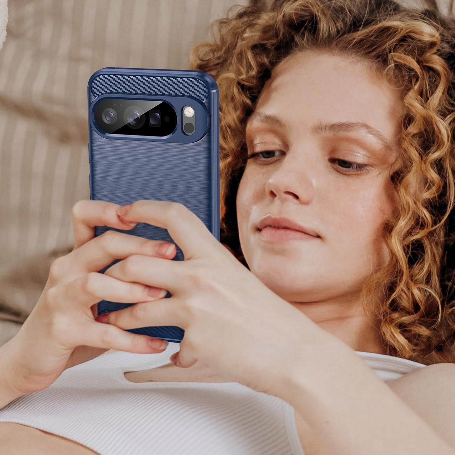 Eine junge Frau mit lockigem Haar betrachtet ein Telefon in einer blauen Hülle. Sie hält das Telefon mit beiden Händen.