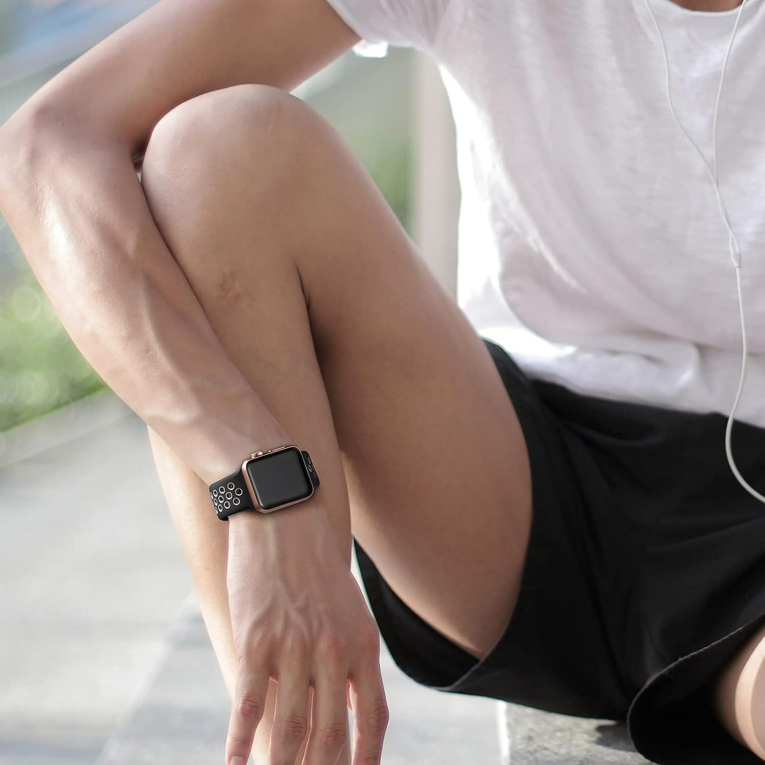 Person trägt eine Uhr mit schwarzem Armband und goldenem Gehäuse. Sie sitzt und trägt ein weißes Hemd und schwarze Shorts. Kopfhörer in den Ohren.
