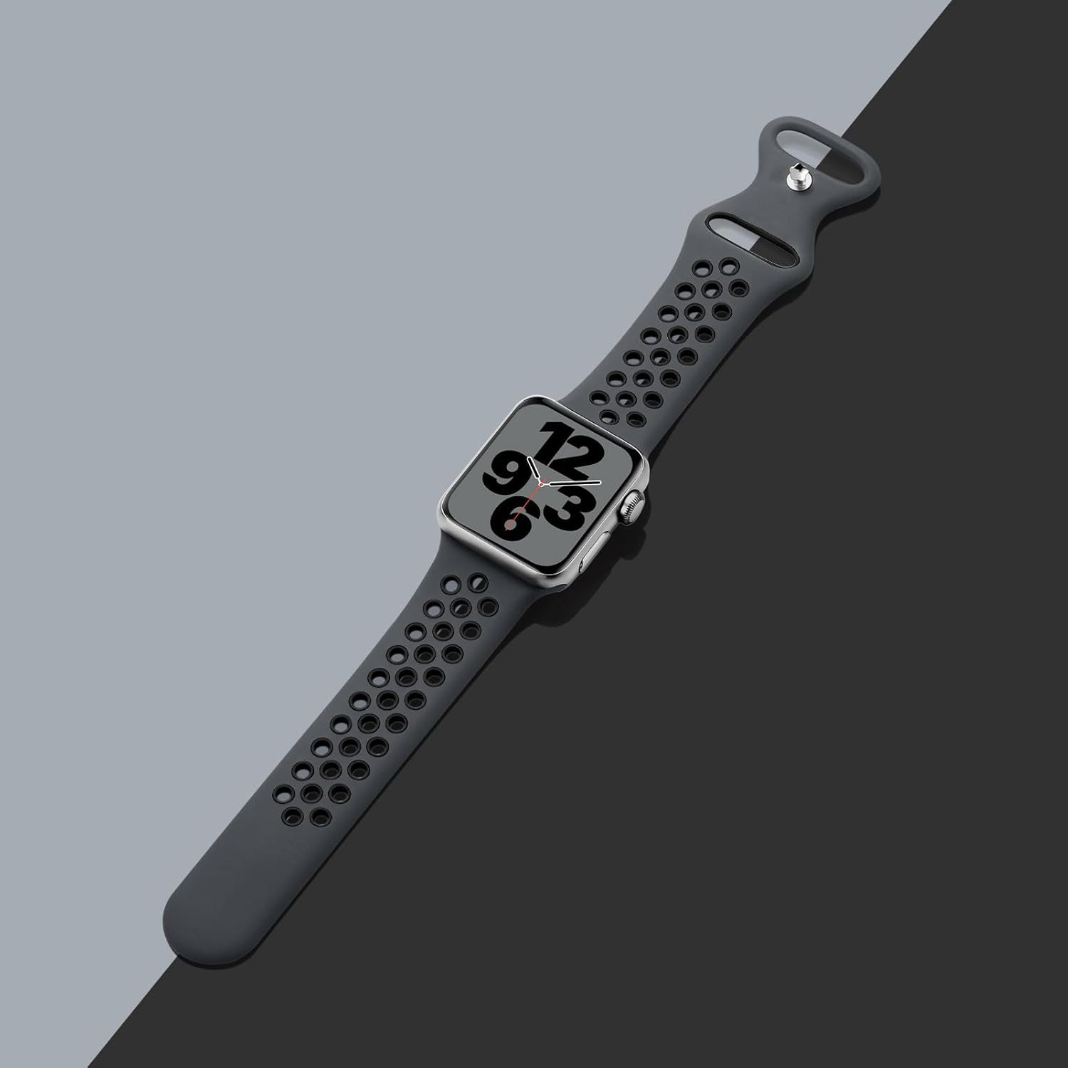 Eine graue Apple Watch mit dunkelgrauem Armband. Die Uhr zeigt die Uhrzeit an. Der Hintergrund ist in graue und schwarze Bereiche unterteilt.