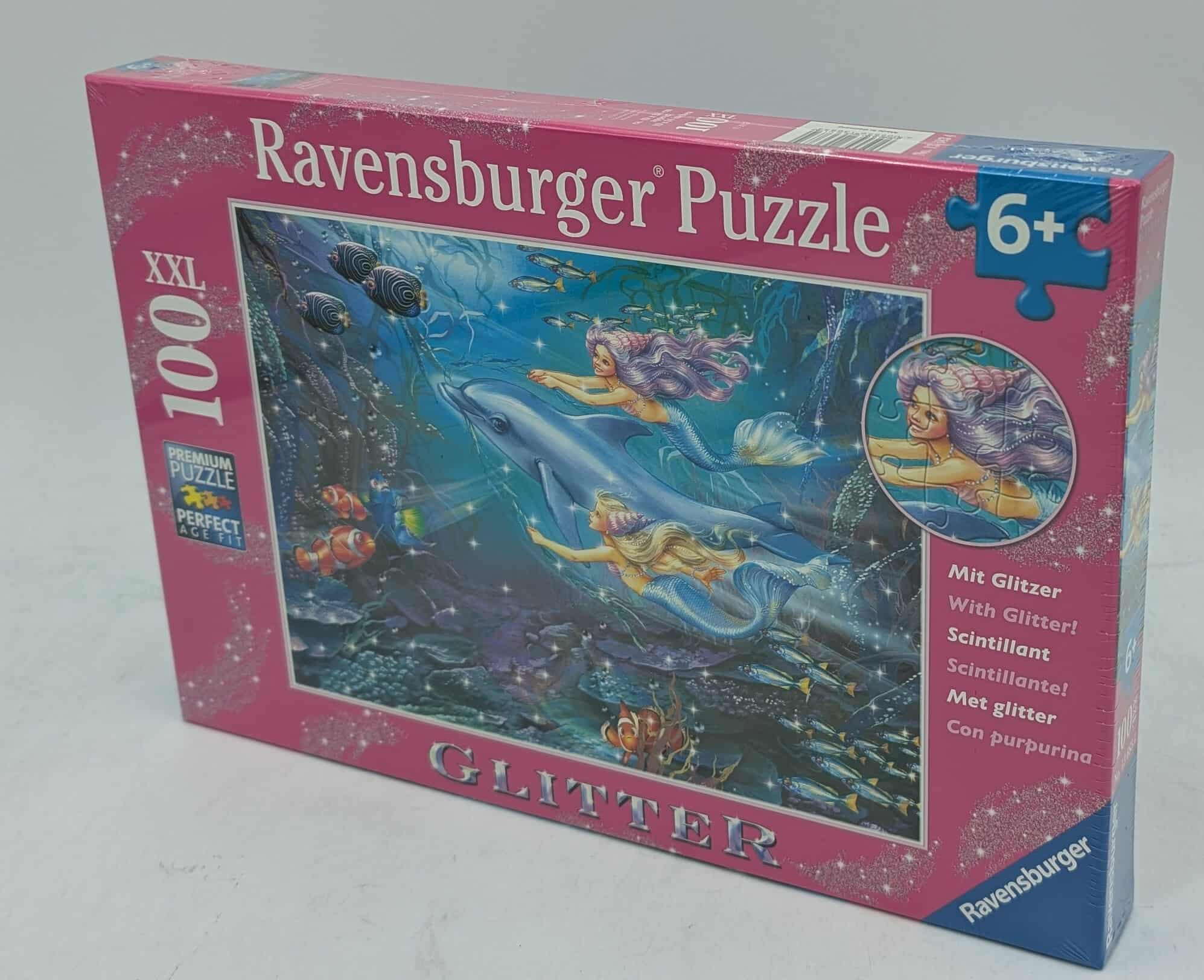 Puzzleschachtel zeigt Meerjungfrauen, die mit Delfinen im Ozean schwimmen. Die Schachtel ist rosa und hat das Ravensburger-Logo.