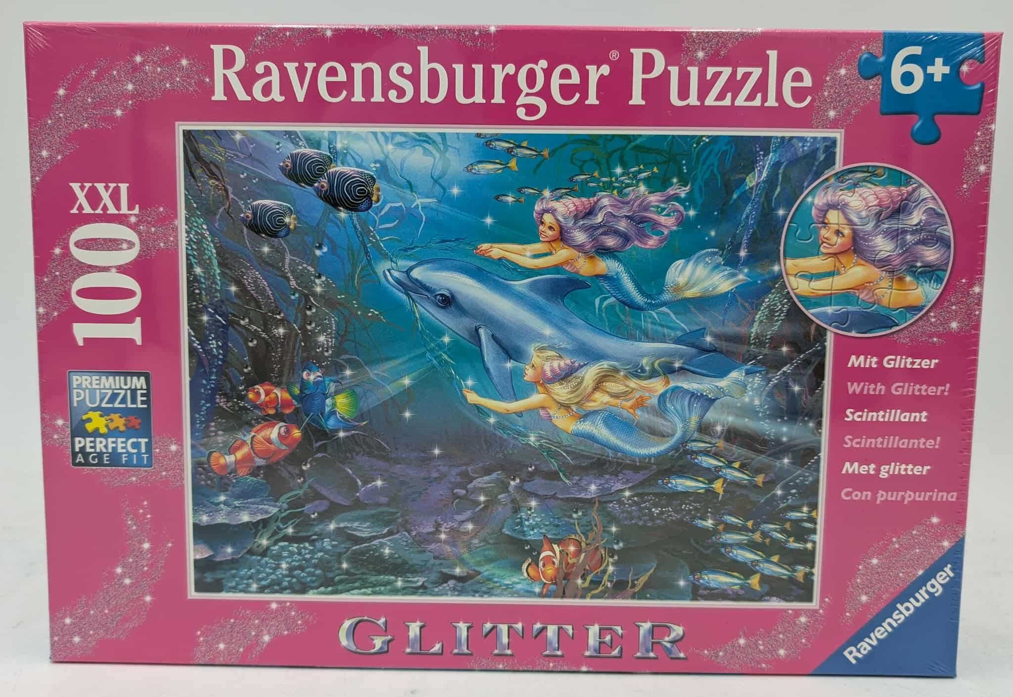 Puzzledose zeigt Meerjungfrauen und einen Delfin, die unter Wasser schwimmen. Fische schwimmen um sie herum. Die Box ist rosa, mit dem Text 'Ravensburger Puzzle'.
