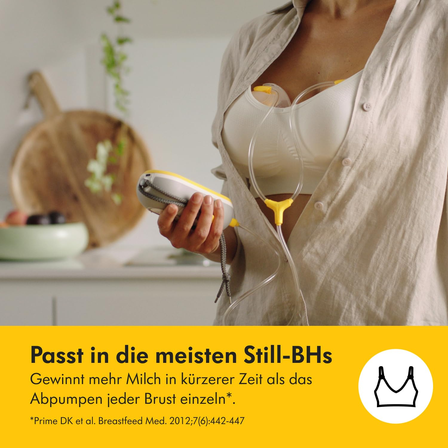 Frau mit Still-BH und Brustpumpe. Sie hält das Pumpgerät. Der Hintergrund zeigt eine Küchenumgebung.