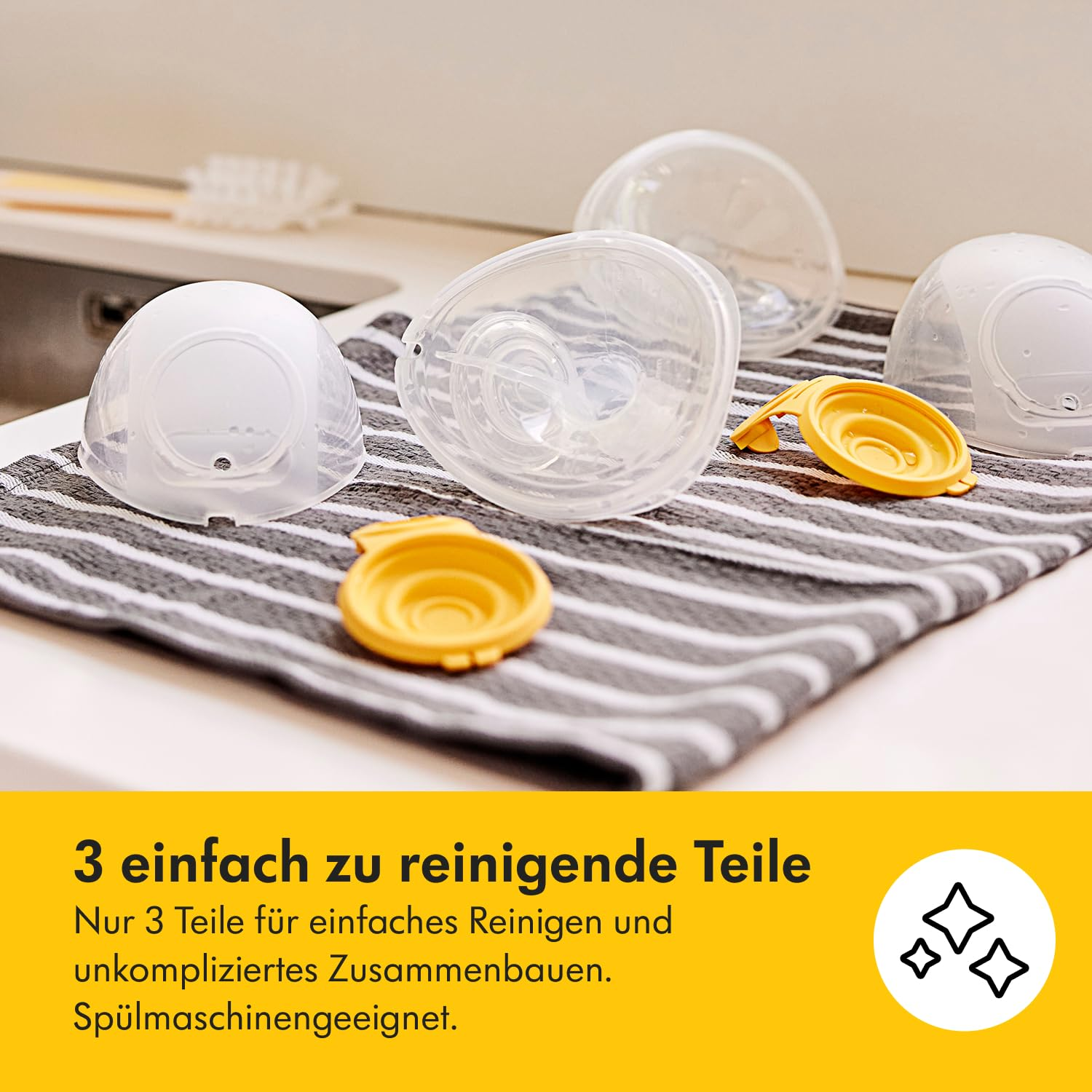 Teile der Milchpumpe auf einem gestreiften Handtuch. Enthält klare und gelbe Kunststoffkomponenten. Hintergrund ist eine Küchenarbeitsplatte.