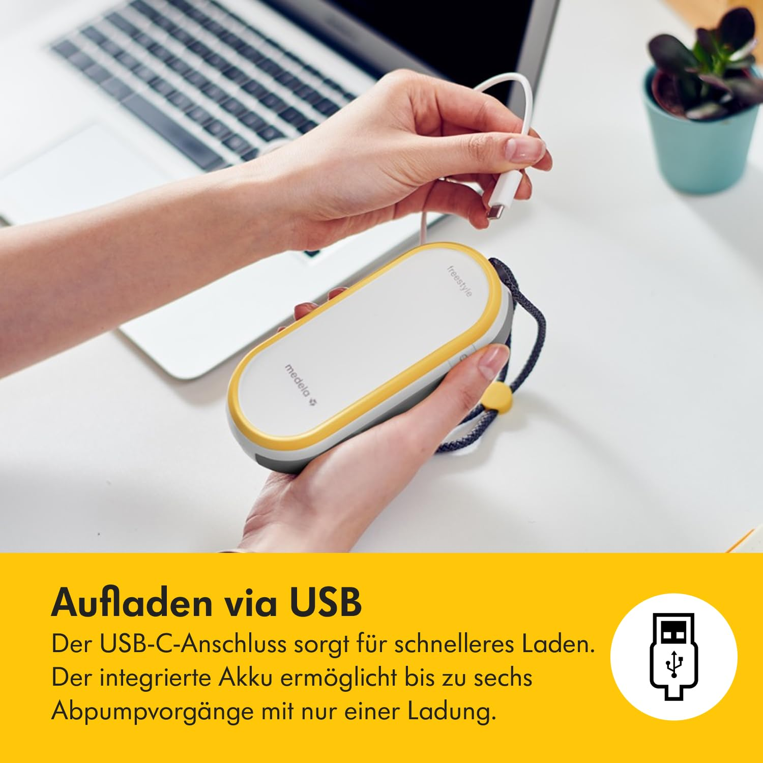 Eine Person hält ein USB-Kabel, das mit einem weiß-gelben Gerät, einem Laptop und einer kleinen Pflanze in einem blauen Topf verbunden ist.