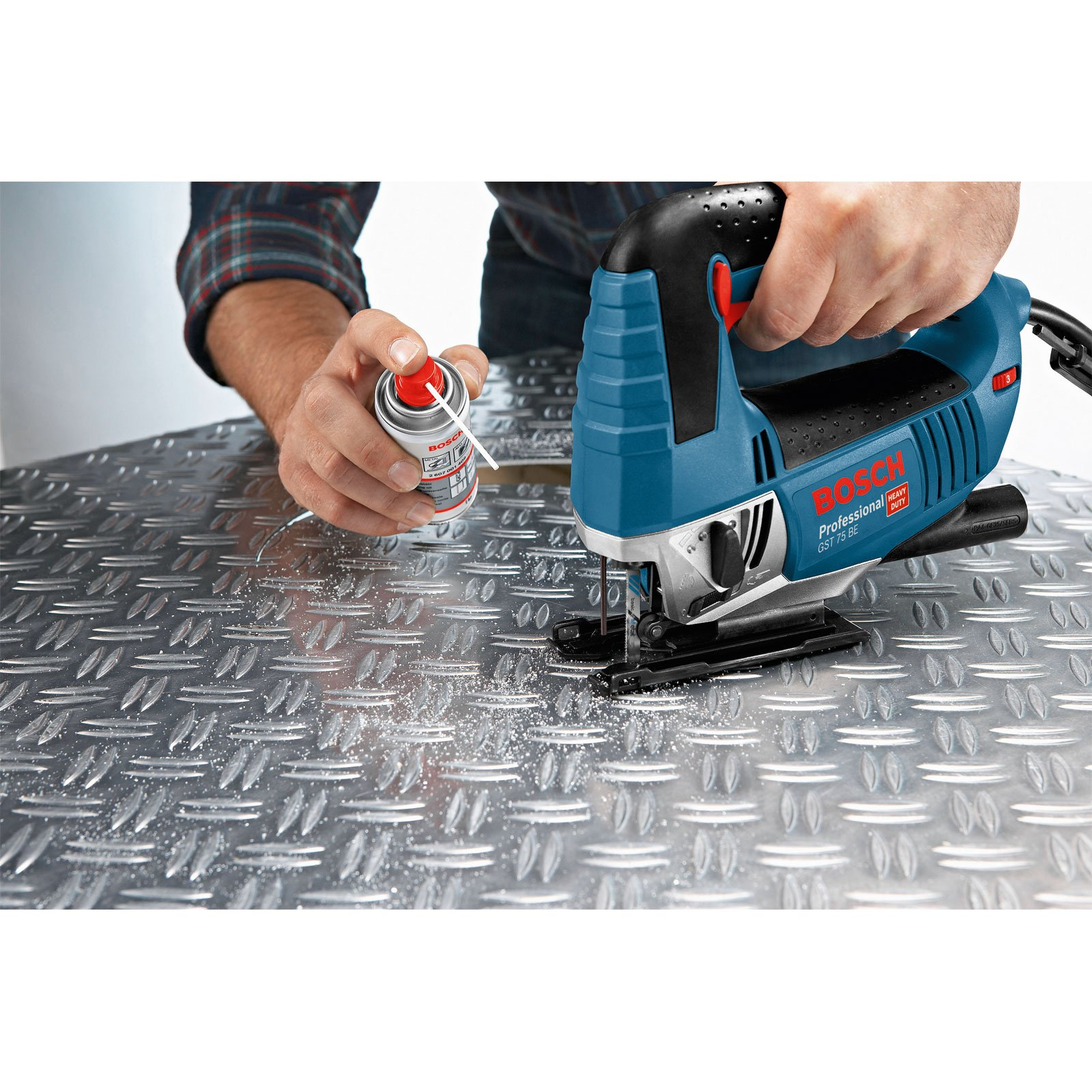 Osoba używa sprayu i niebieskiej wyrzynarki na metalowej powierzchni. Widoczne trociny.