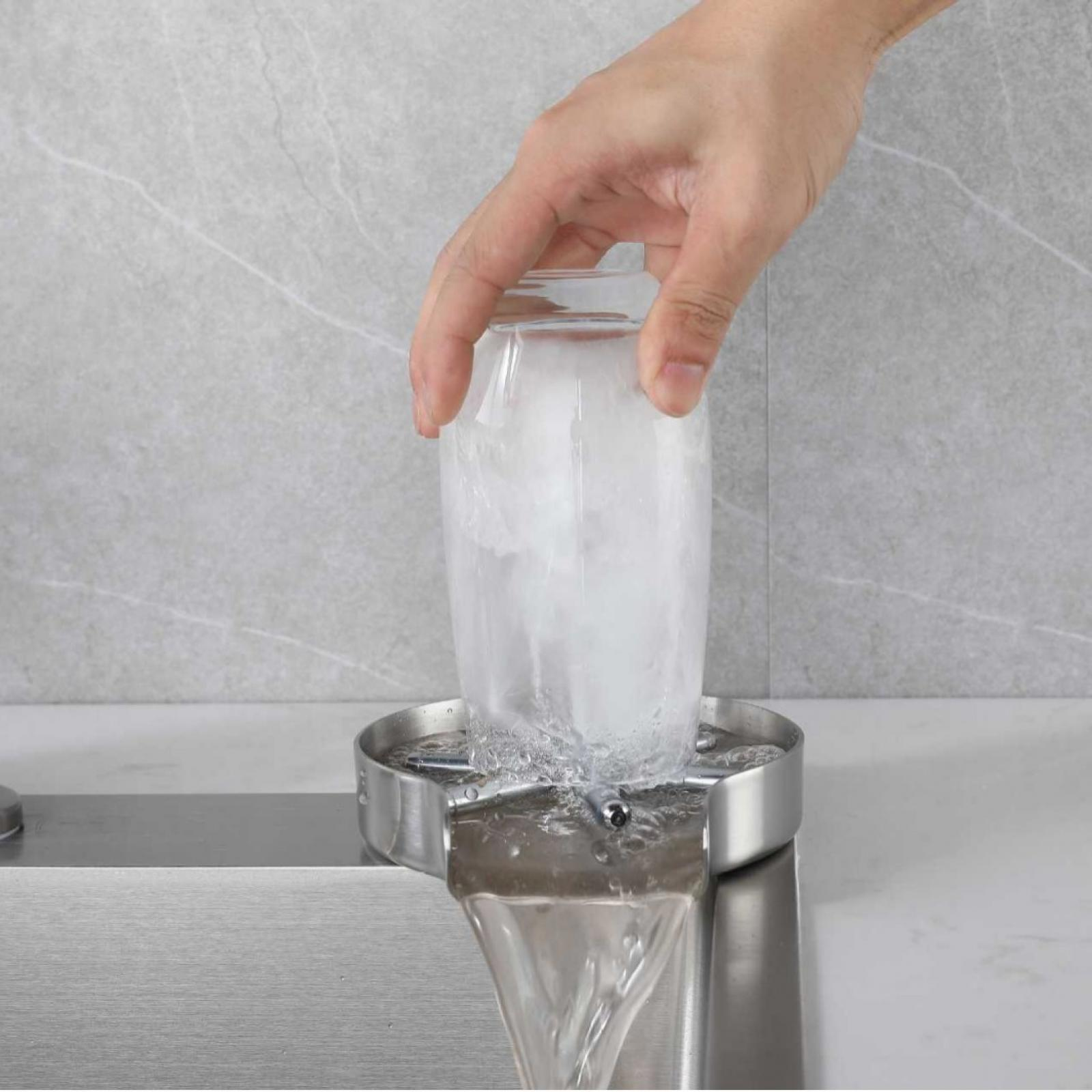 Hand hält ein mit Eis gefülltes Glas über einem Edelstahlbecken. Wasser fließt aus dem Glas in das Becken.