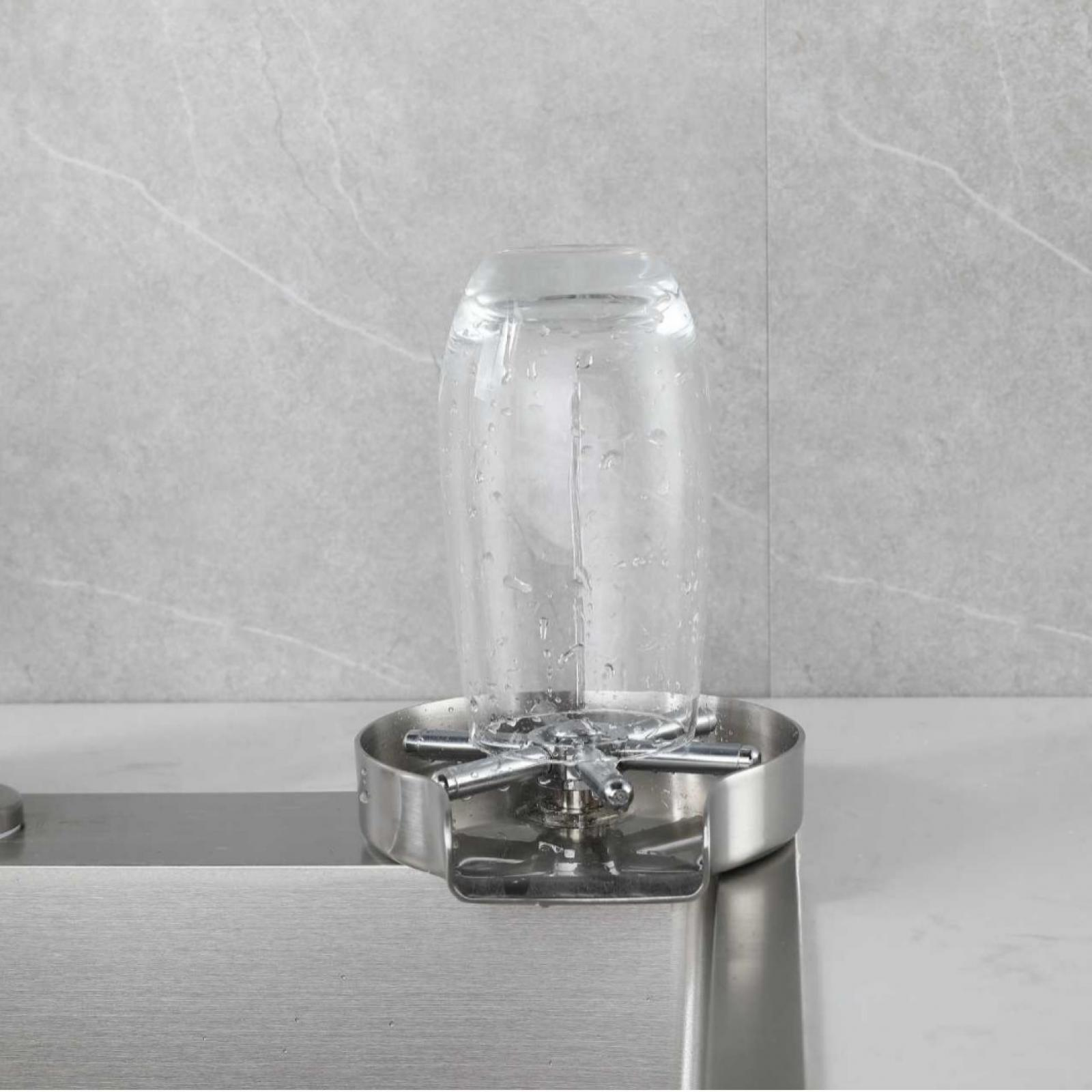 Ein klares Glas steht in einem Edelstahlspüler. Wassertropfen bedecken das Glas. Grauer gefliester Hintergrund.