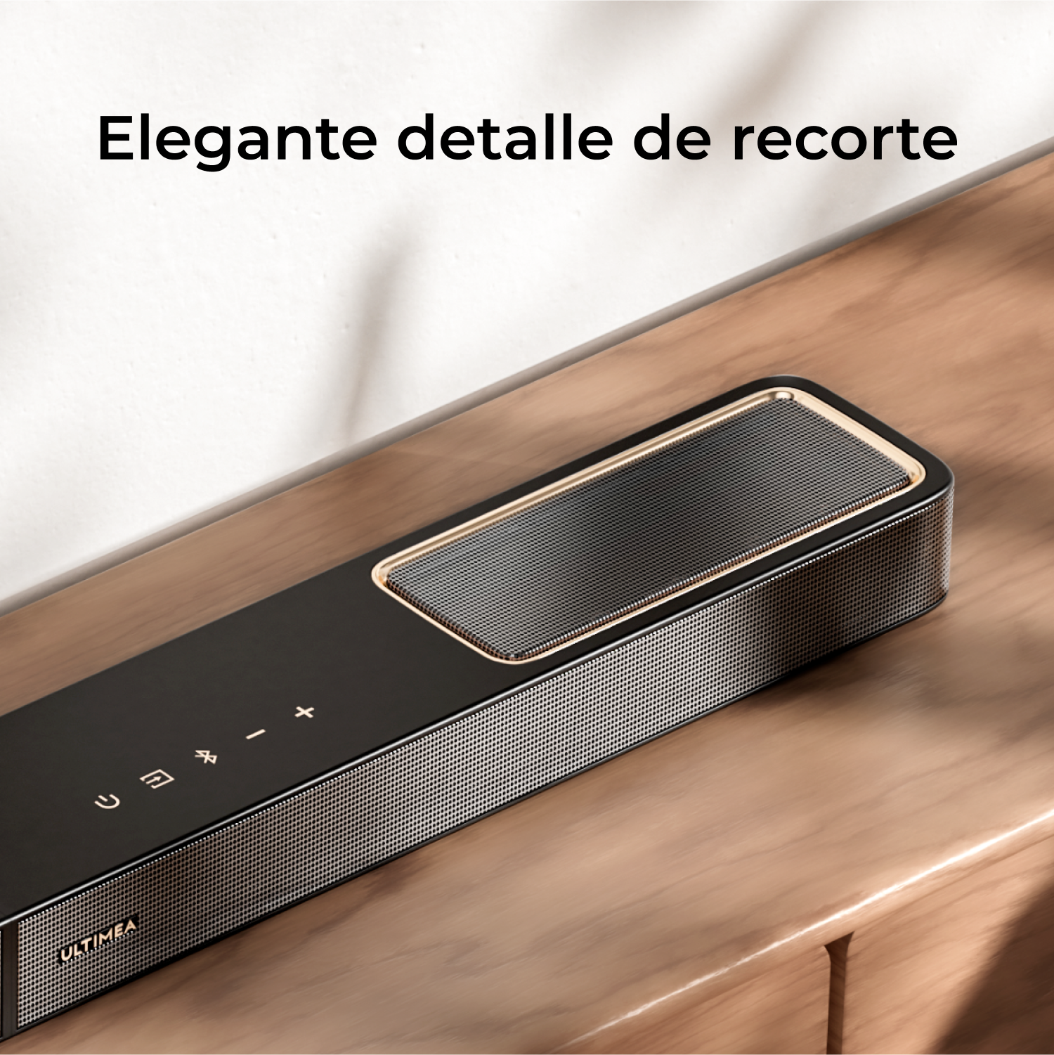 Una barra de sonido negra con malla plateada, ribete dorado y botones de control. Se encuentra sobre una superficie de madera con texto: Elegante detalle de recorte.