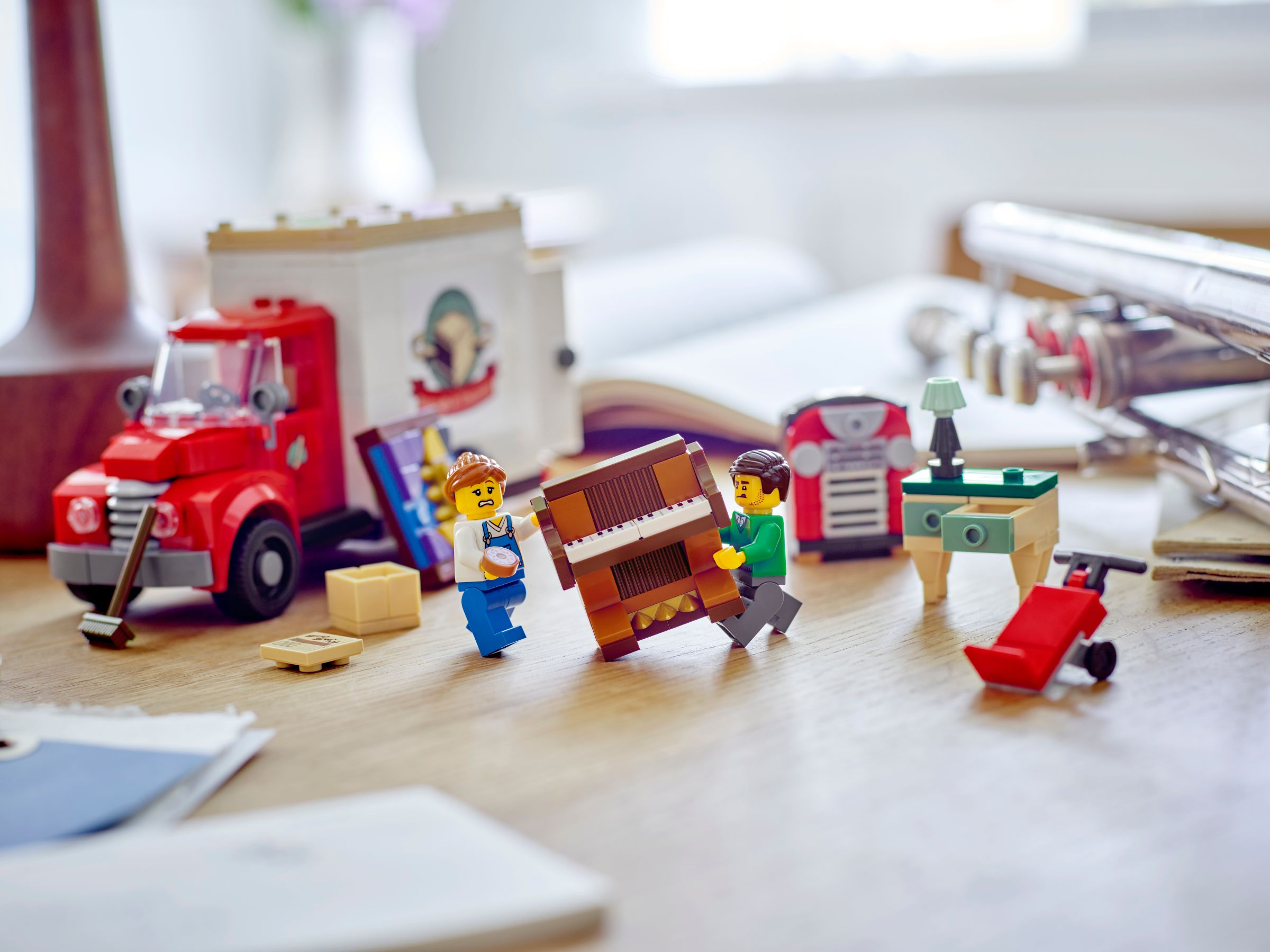 Lego-Szene mit Miniaturfiguren, die ein Klavier bewegen. Enthält einen roten LKW, einen kleinen Tisch, ein Radio und einen Handwagen.