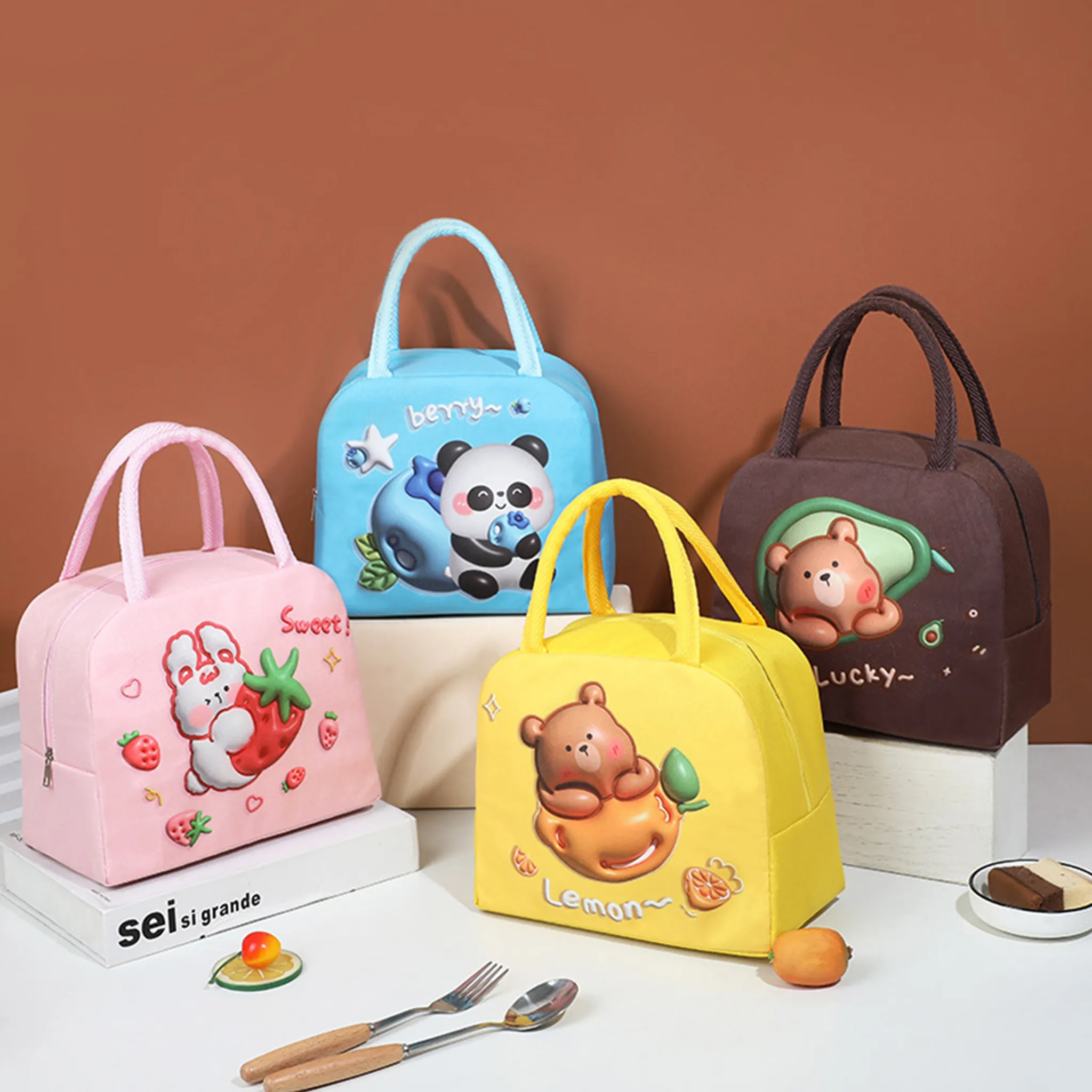 Vier Lunchpakete mit Cartoon-Designs. Rosa Tasche mit Hase & Erdbeere, blau mit Panda, gelb mit Bär und braun mit Bär in Avocado.