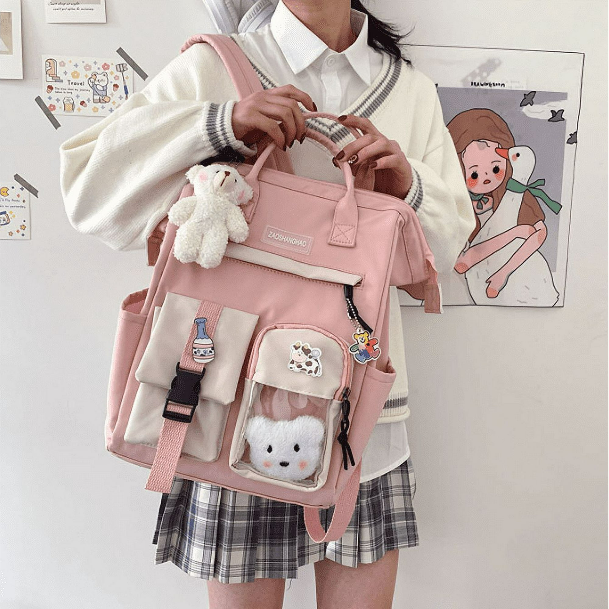 Eine Person hält einen rosa Rucksack mit Taschen und angebrachten Anhängern. Ein weißer Teddybär-Schlüsselanhänger hängt an der Tasche.