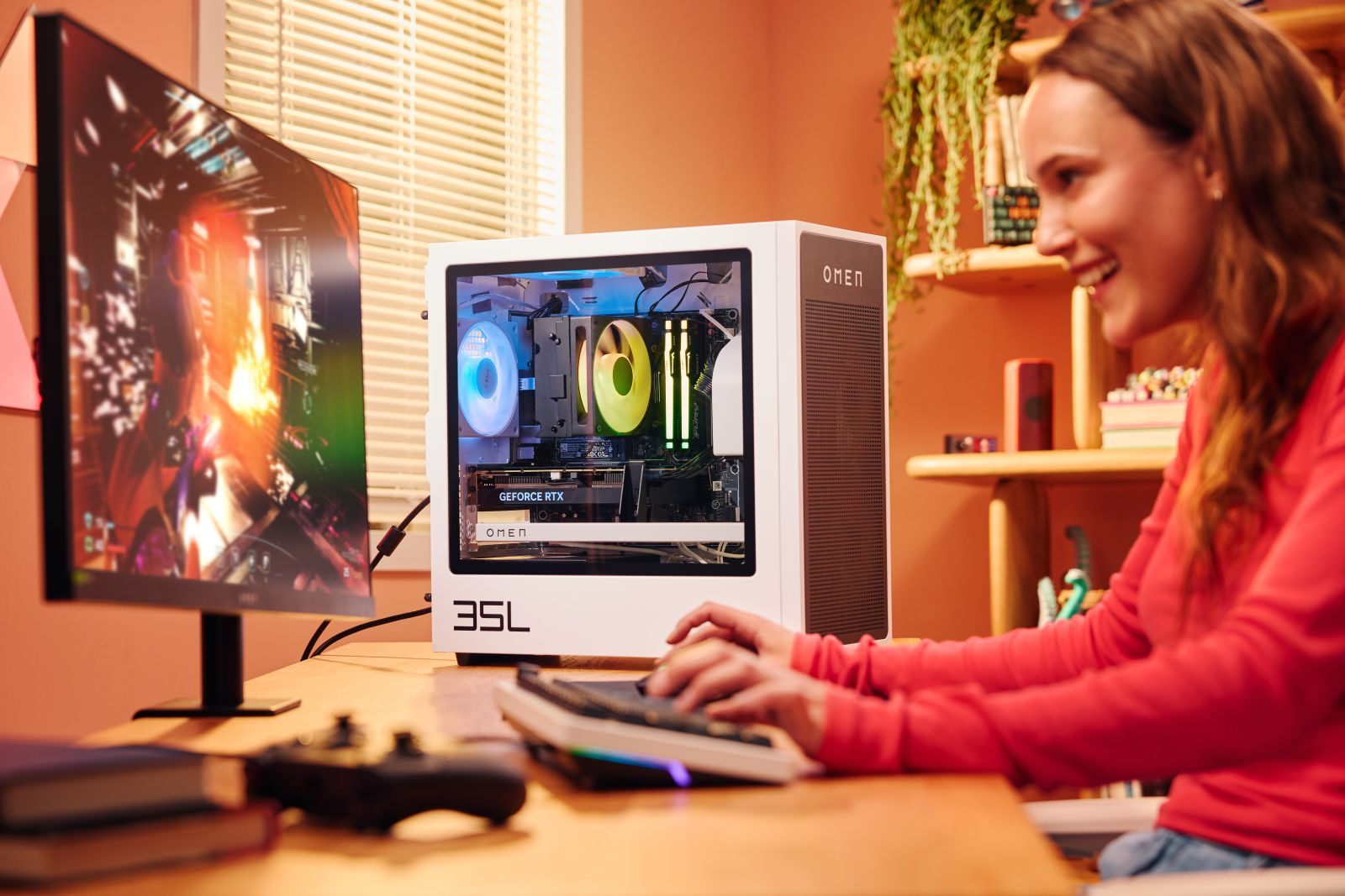 Kobieta w czerwieni gra na komputerze. Biały komputer OMEN z kolorowymi światłami na biurku. Monitor wyświetla nagrania z gry.